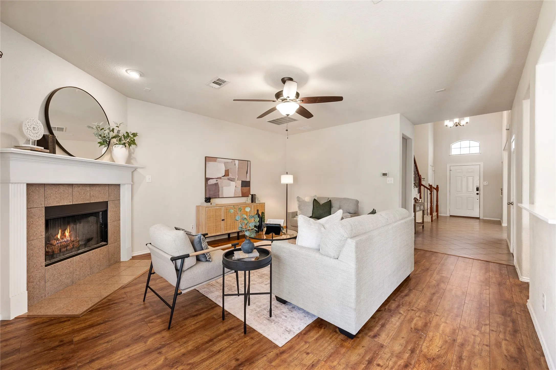 Living area featuring wood-finish flooring, a corner fireplace with a white mantel, and a ceiling fan
