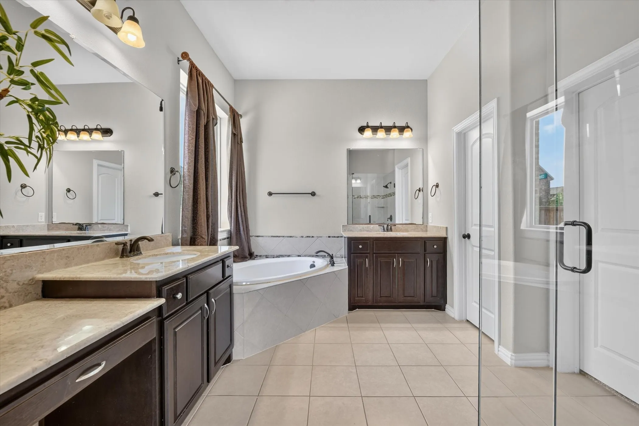 Dual vanities with stone countertops, corner soaking tub, tile flooring, and glass-enclosed shower