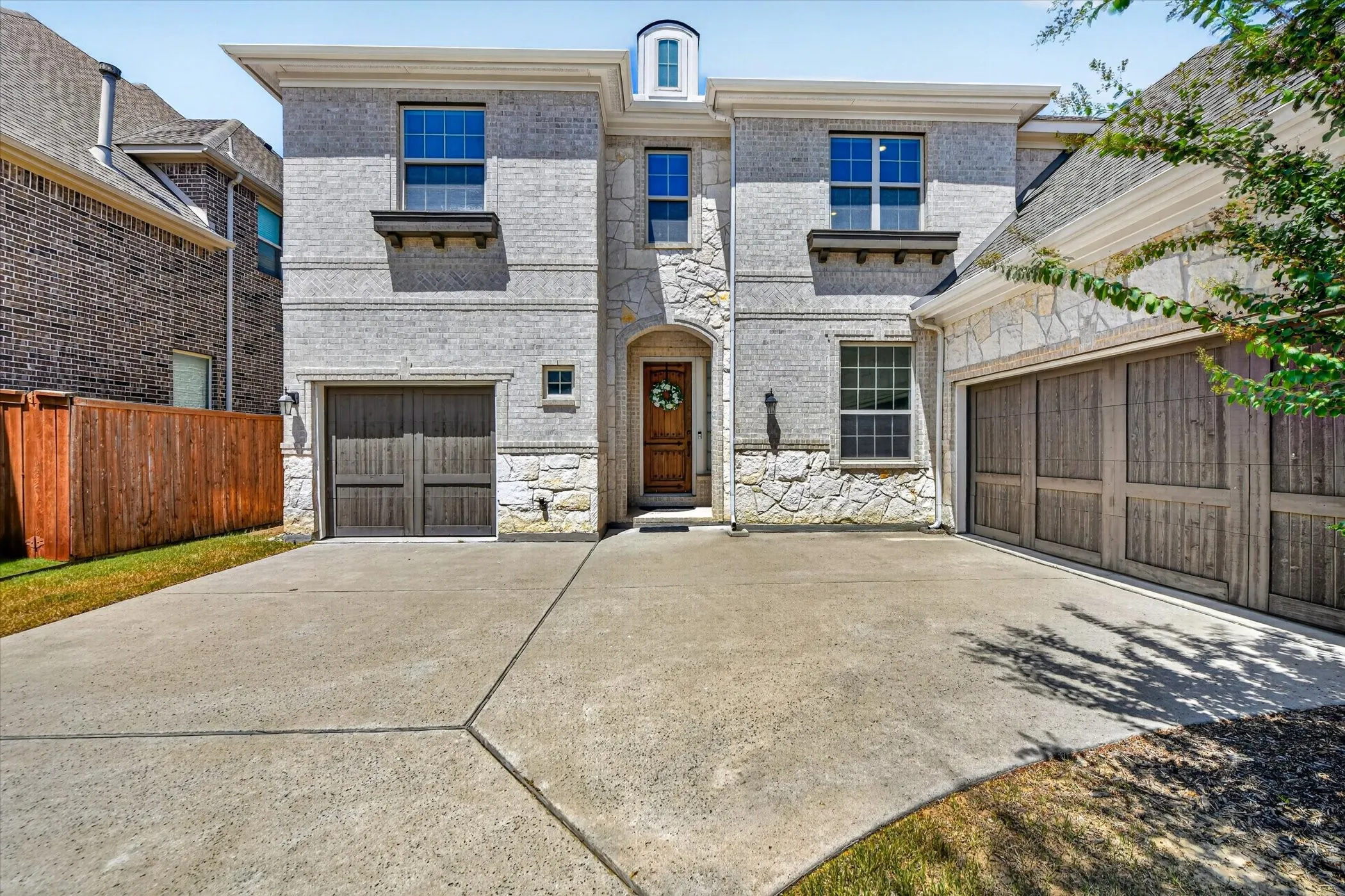 Stone and brick facade with multiple windows, featuring two garage doors with wood-finish panels and a central arched entry