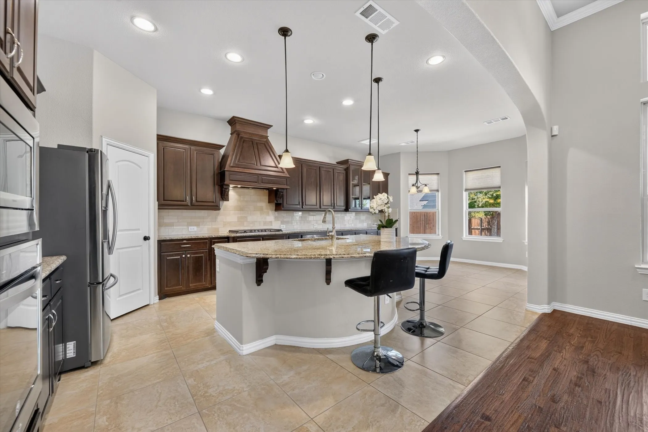 Kitchen featuring an expansive island with a stone-finish countertop, dark wood cabinetry, a decorative range hood, and tile flooring
