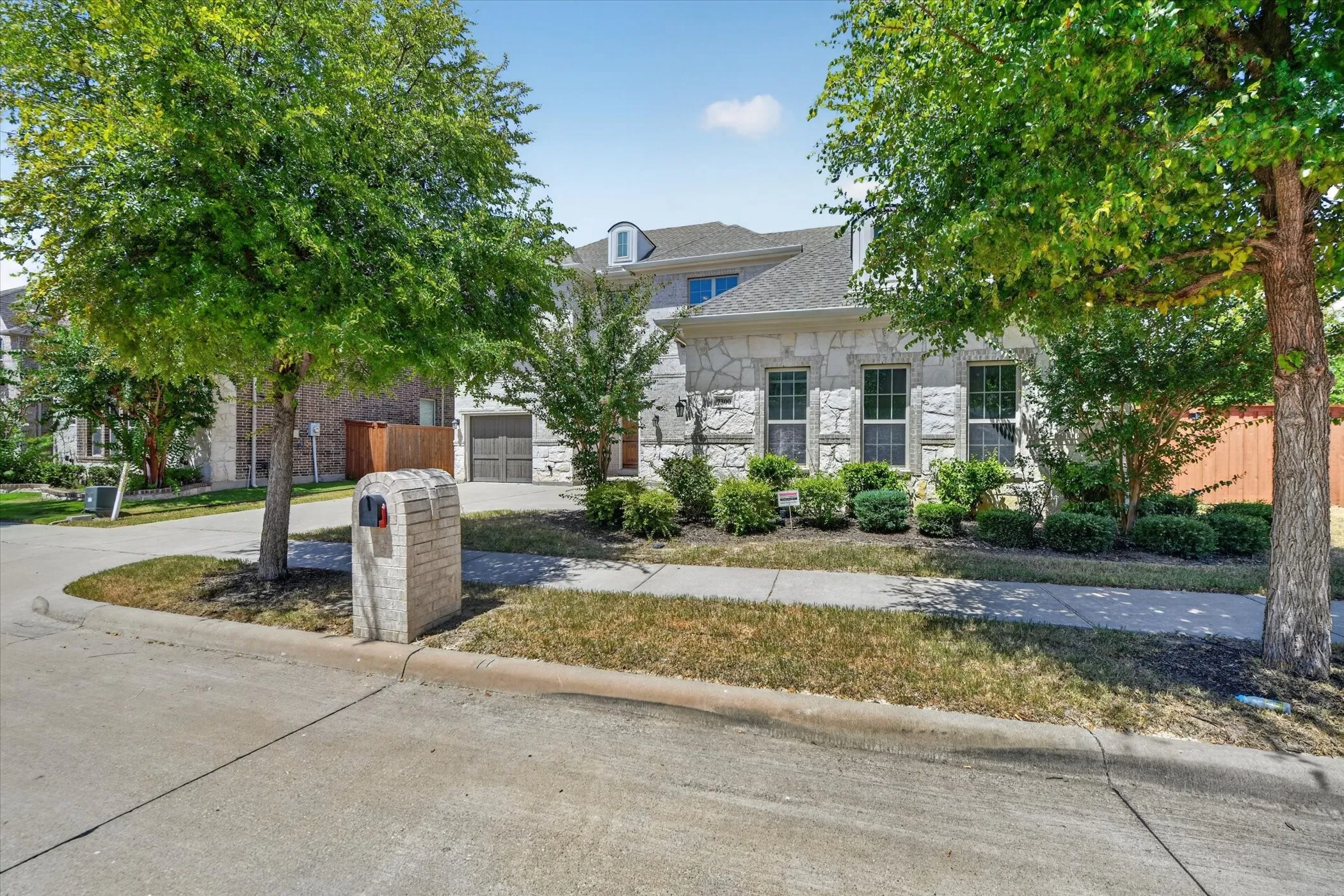 Stone exterior with integrated garage, mature trees, and landscaped shrubbery