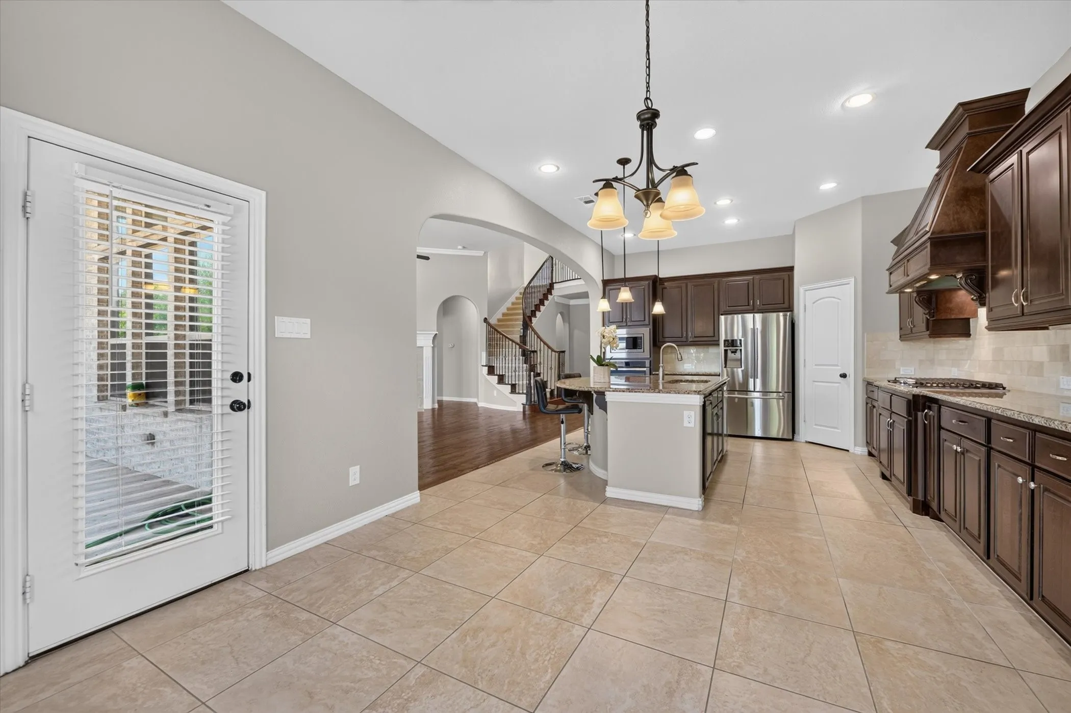 Well-appointed kitchen featuring dark wood cabinetry, stainless steel appliances, a center island with seating, pendant lighting, and tiled flooring