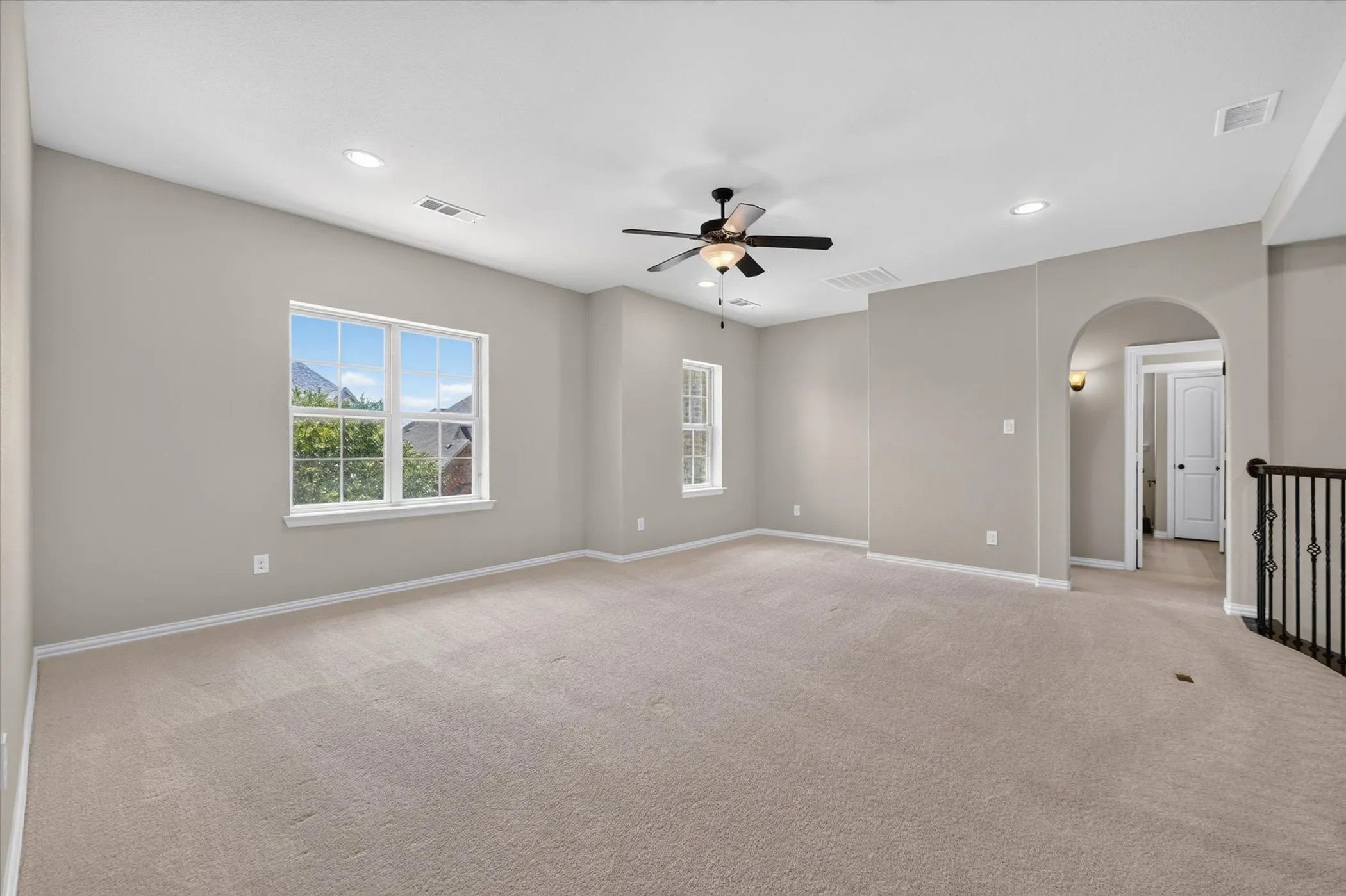 Expansive carpeted room featuring multiple windows, a ceiling fan with integrated lighting, recessed lighting, and an arched doorway