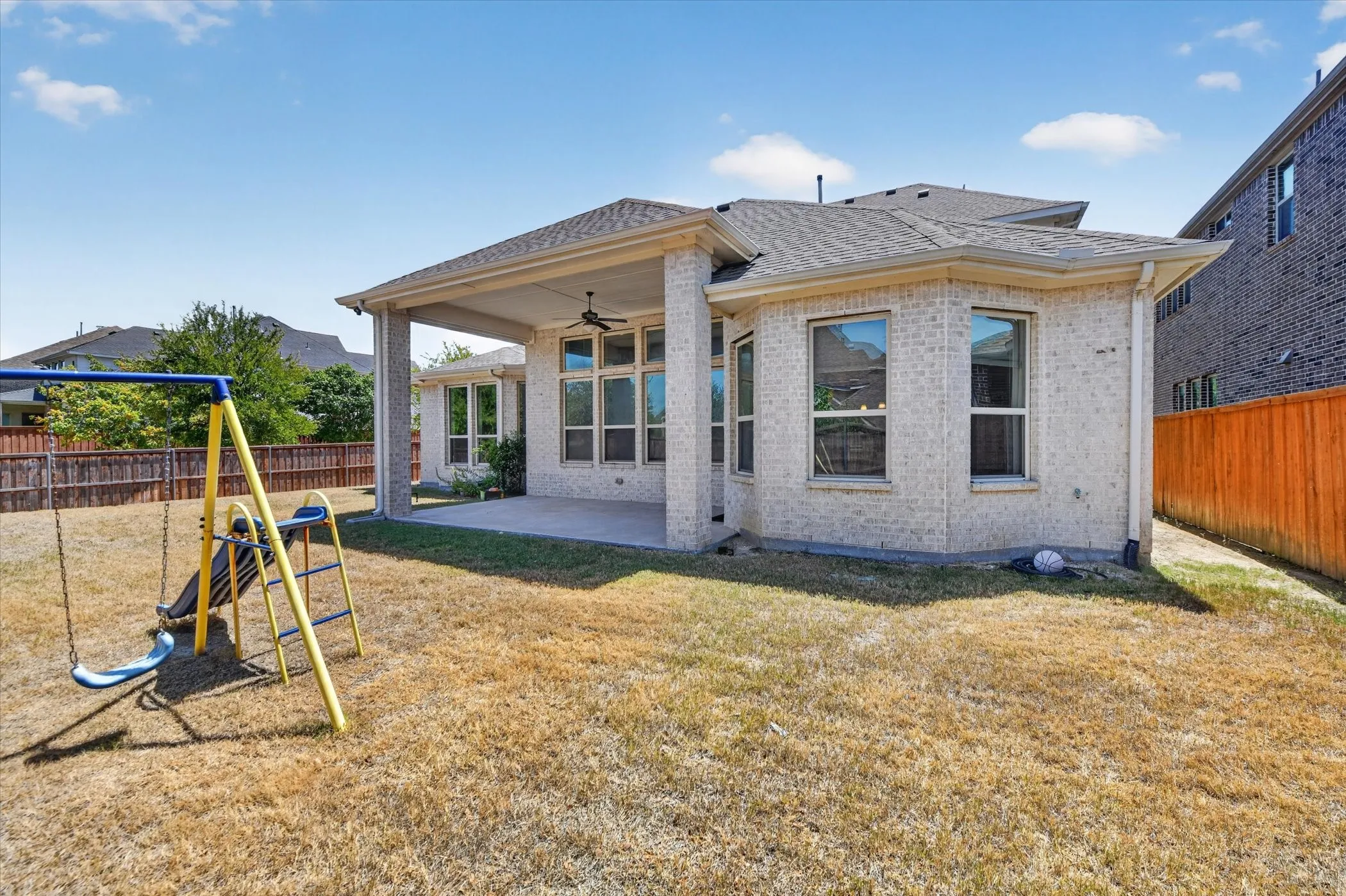 Expansive backyard featuring a covered patio, ceiling fan, and privacy fencing
