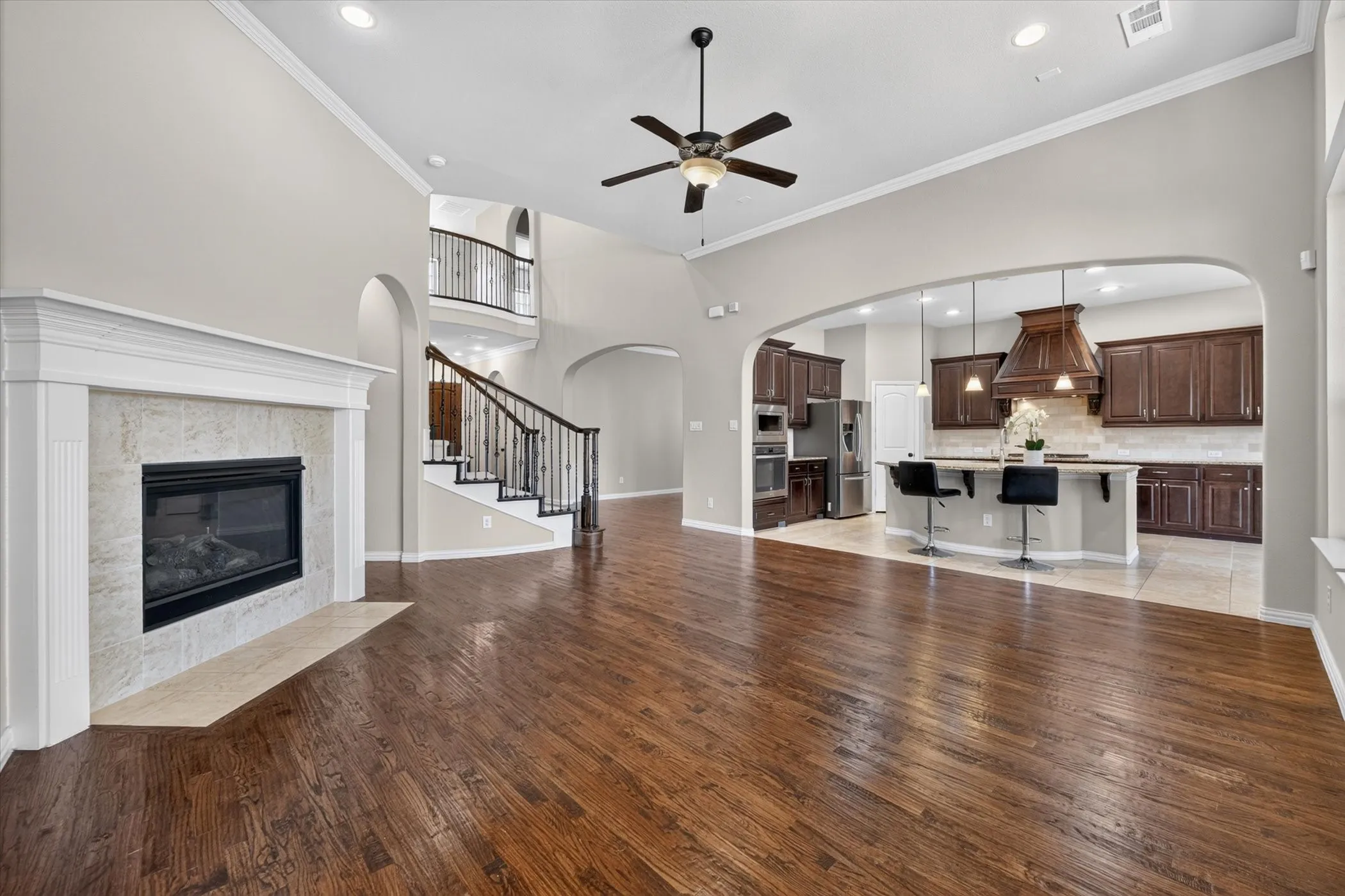 High vaulted ceilings, fireplace with tile surround, wood-finish flooring, staircase with wrought iron balusters, and a kitchen featuring a central island with pendant lighting