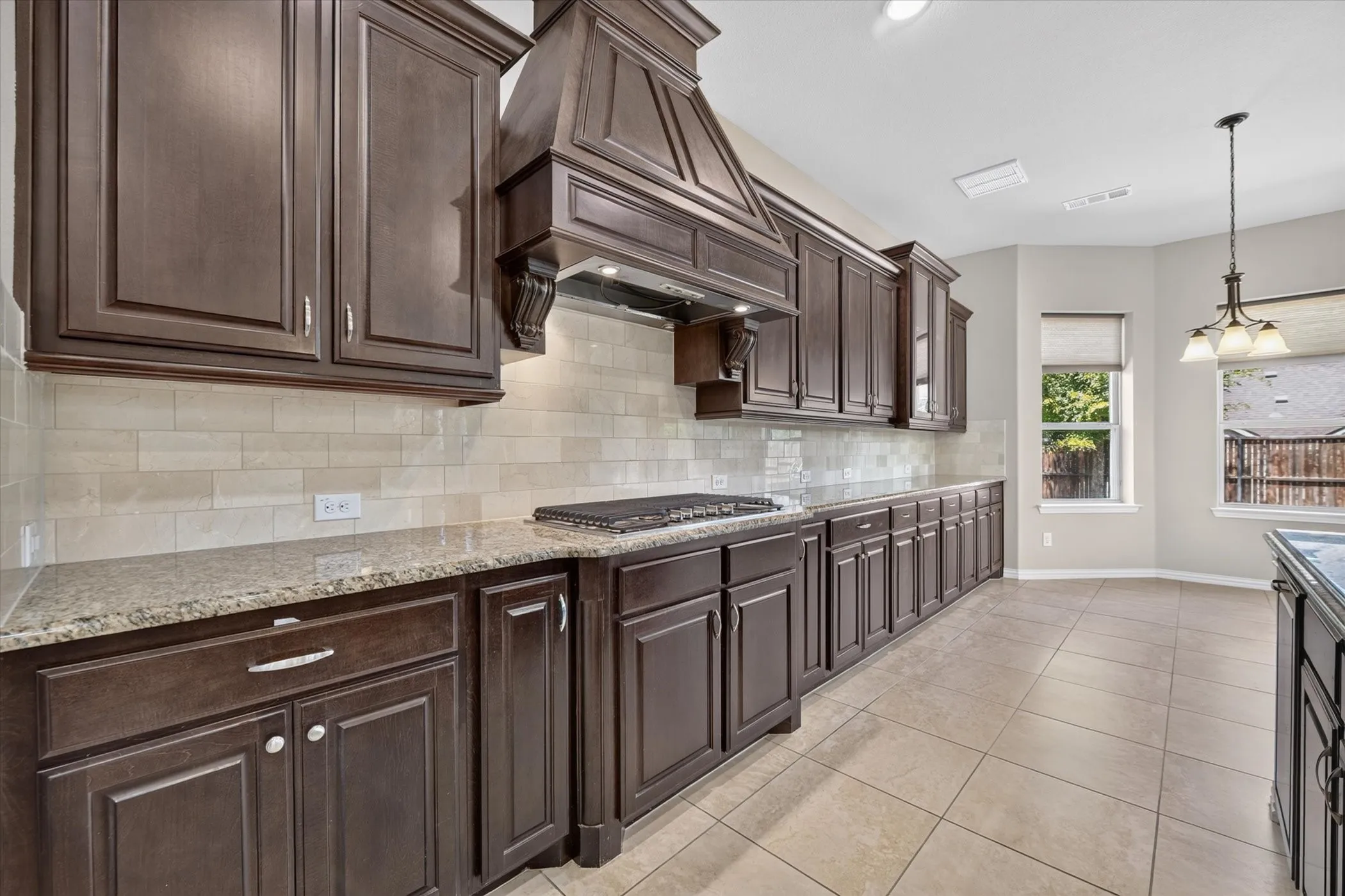 Expansive cabinetry with dark wood finish, light-toned tile backsplash, and stone countertops