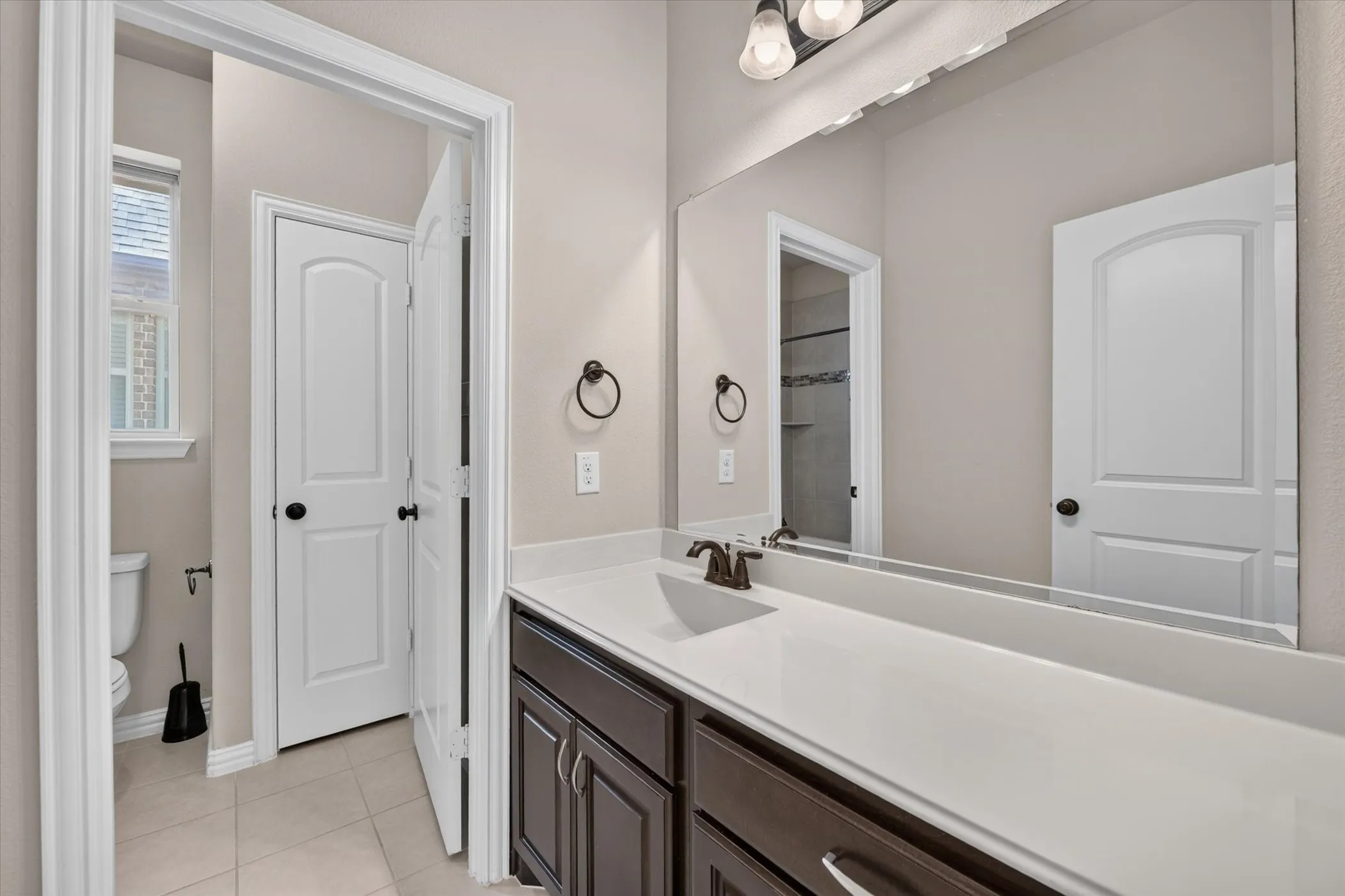 Dual-sink vanity with white countertop, dark wood-finish cabinetry, and bronze-finish fixtures