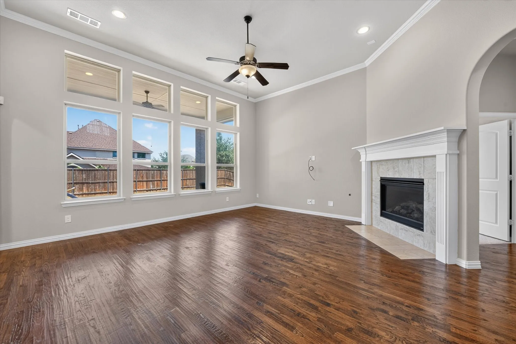 Spacious living area featuring wood-finish flooring, a tiled fireplace with a white mantel, and a multi-pane window arrangement