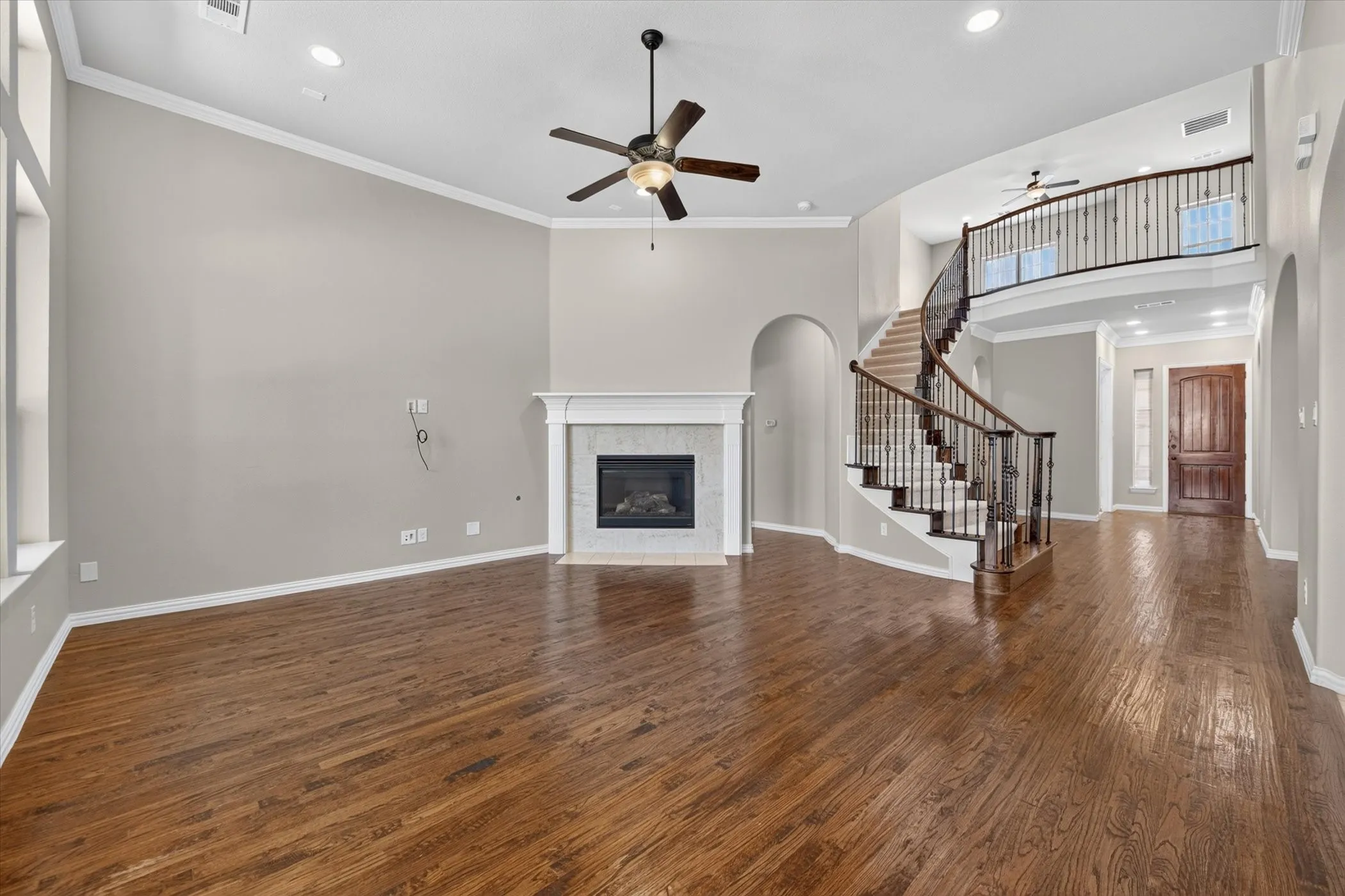 Hardwood flooring throughout, a curved staircase with wrought iron balusters, a decorative fireplace with a mantel, a vaulted ceiling, and recessed lighting