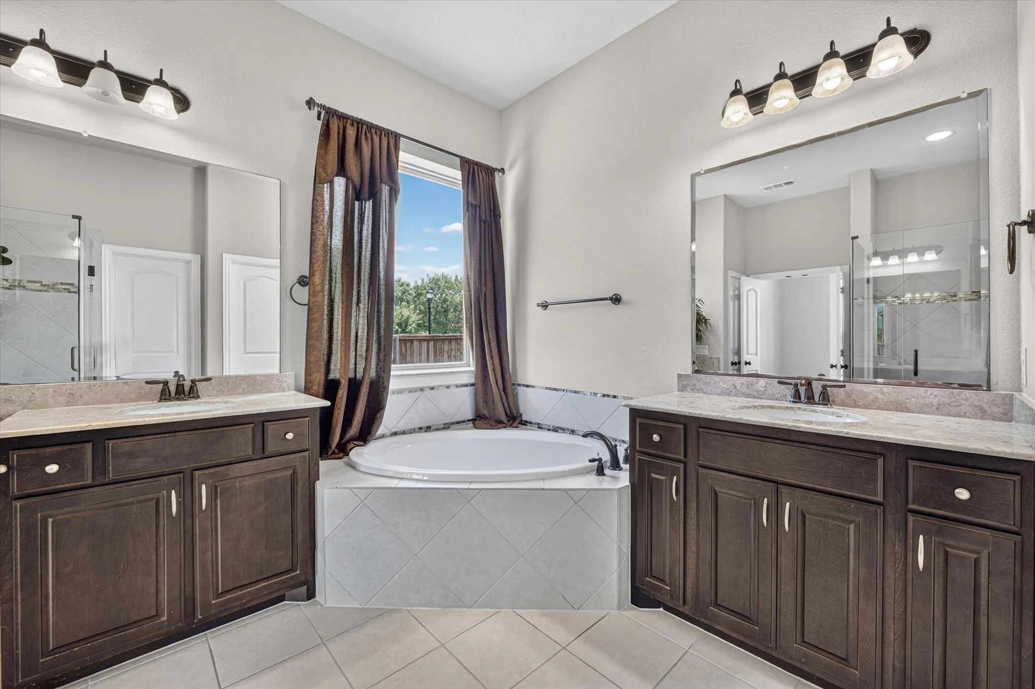 Dual vanities with stone-finish countertops, an oval soaking tub, and a separate glass-enclosed shower