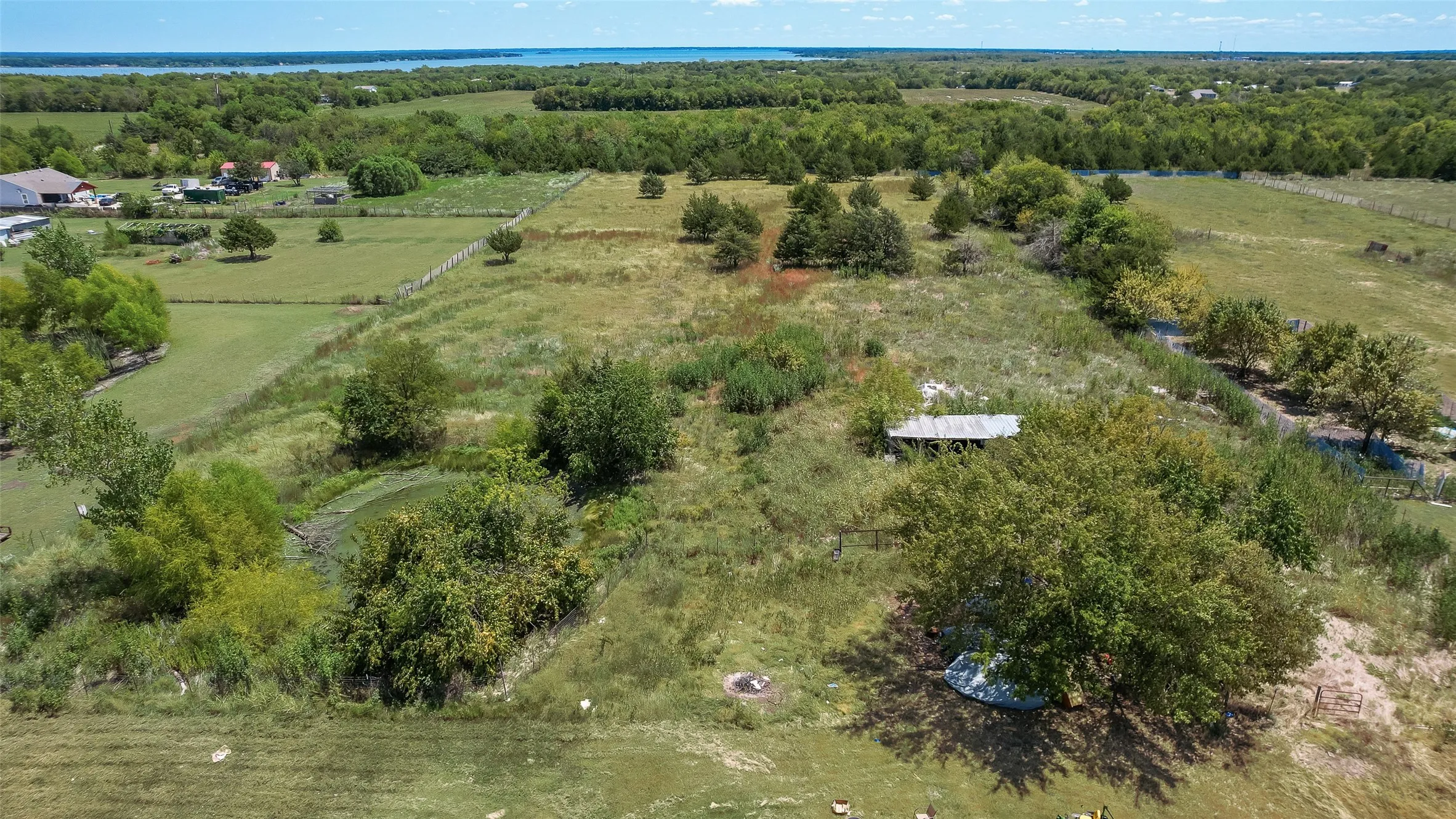 Expansive land parcel featuring open fields, mature trees, and a distant body of water