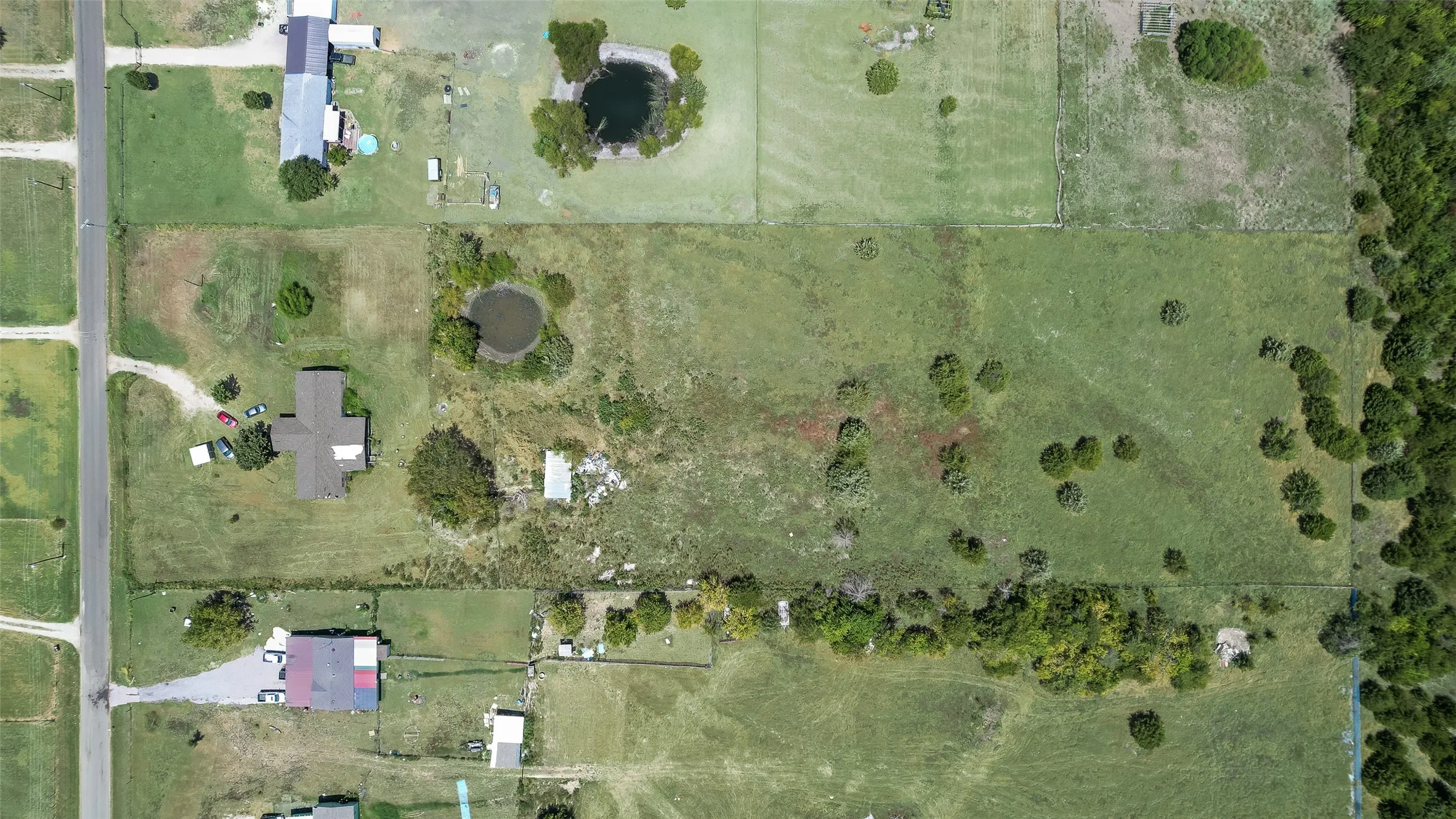 Expansive rural property featuring a main residence, additional structure with a red roof, two distinct ponds, and a densely wooded border