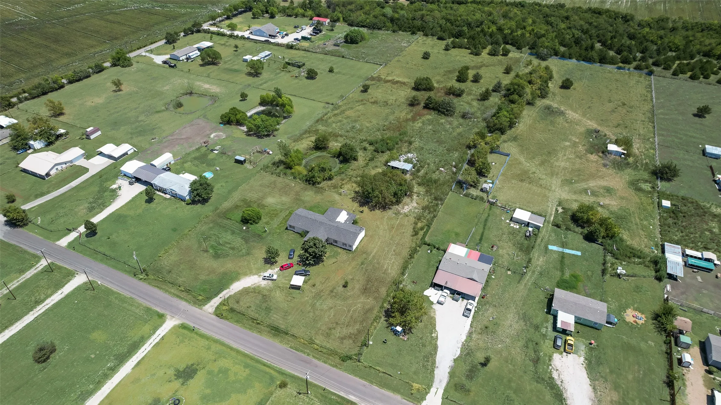 Expansive property featuring multiple structures, open green spaces, and a paved road frontage