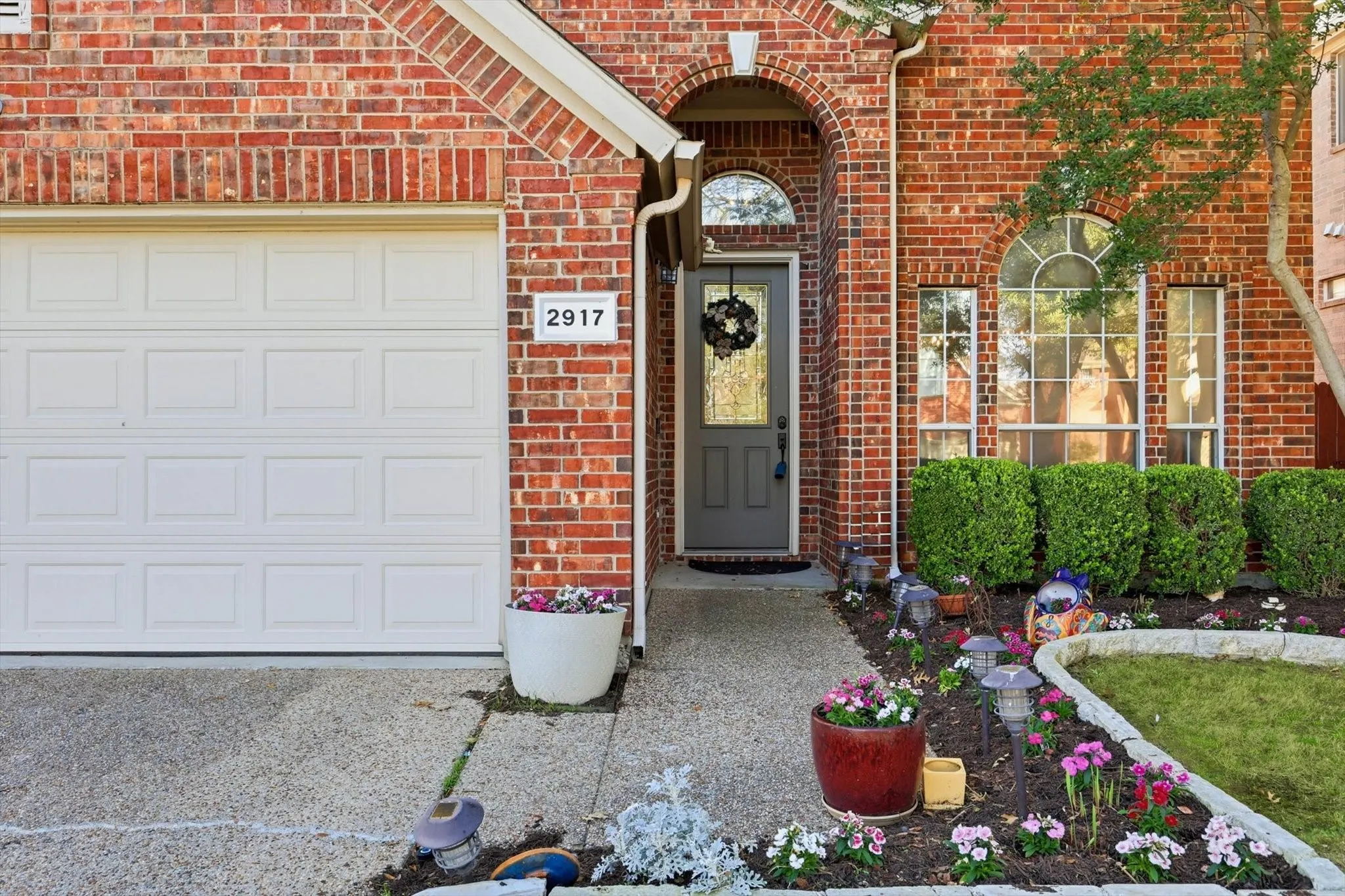 Brick exterior, arched entryway, arched window, shrubbery, landscaped garden beds
