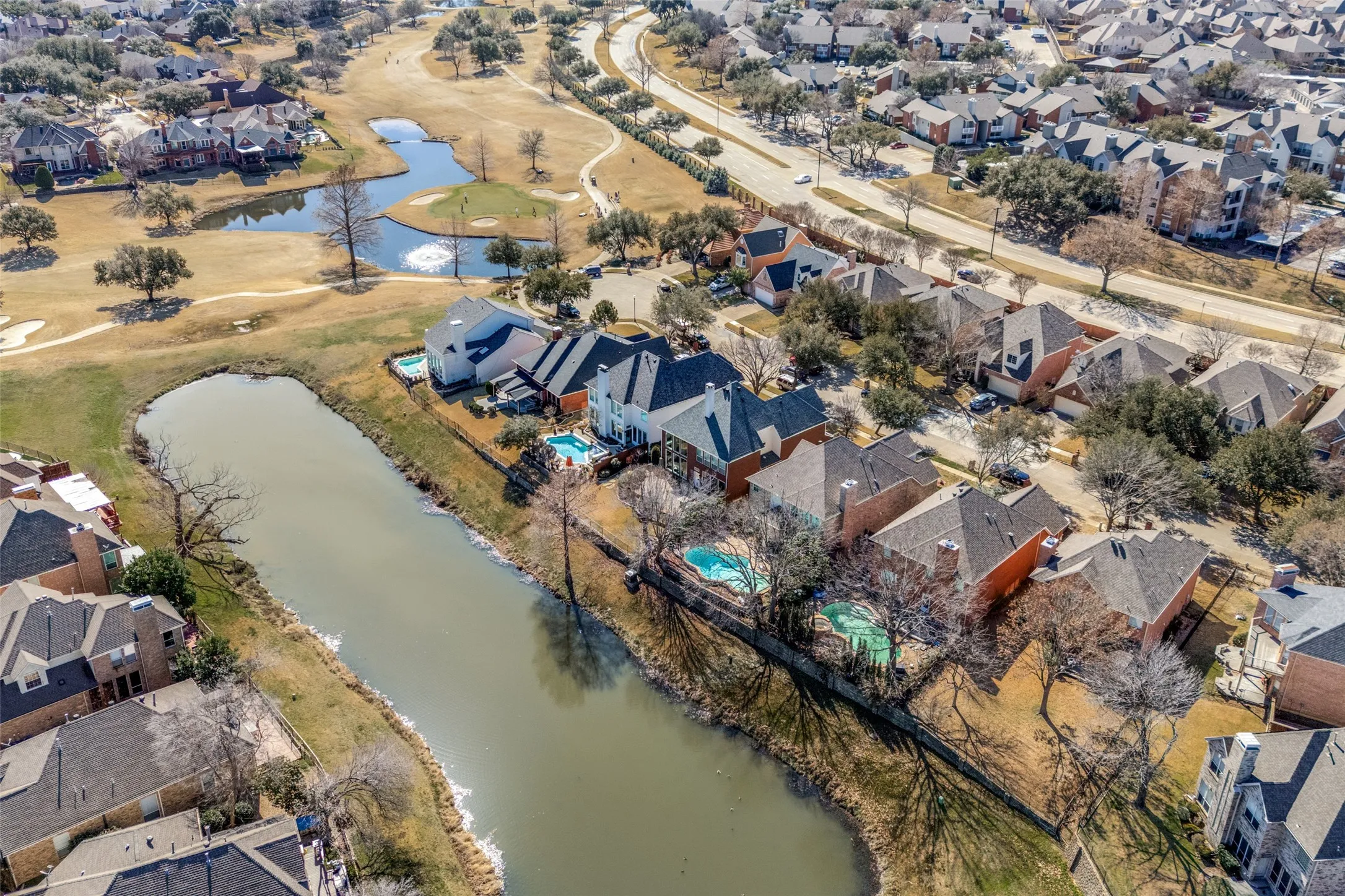 Aerial perspective showcasing a residential community with homes featuring private swimming pools, situated along a waterway, and bordering a golf course with multiple water features