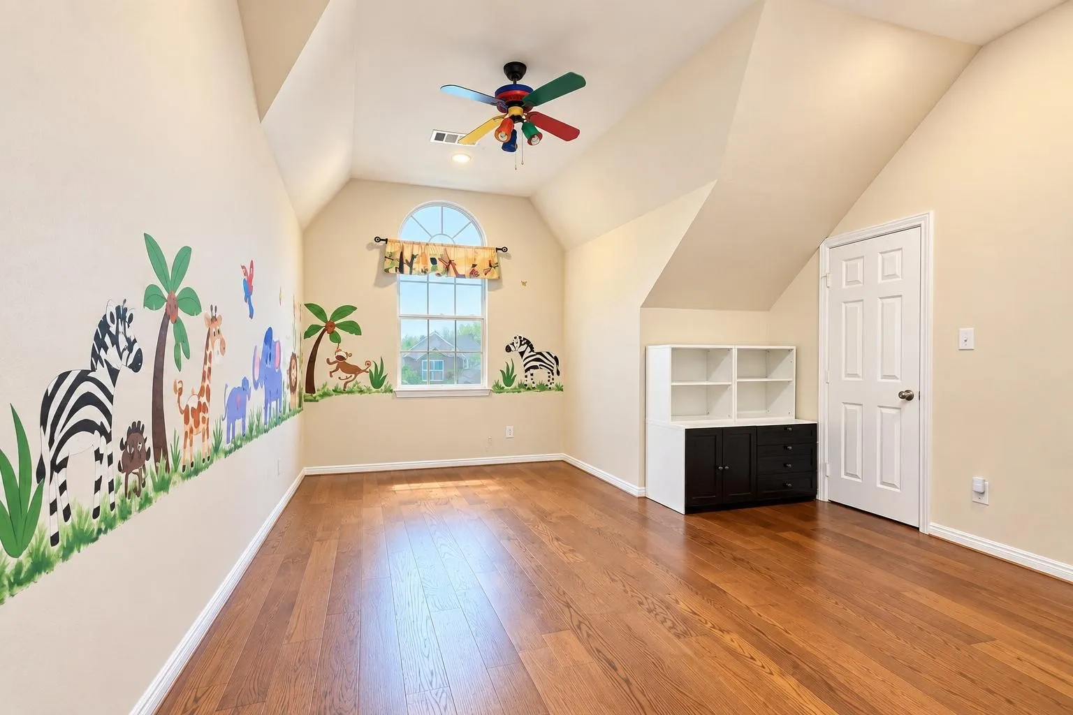 Hardwood flooring with a built-in storage unit, an arched window, and a colorful ceiling fan