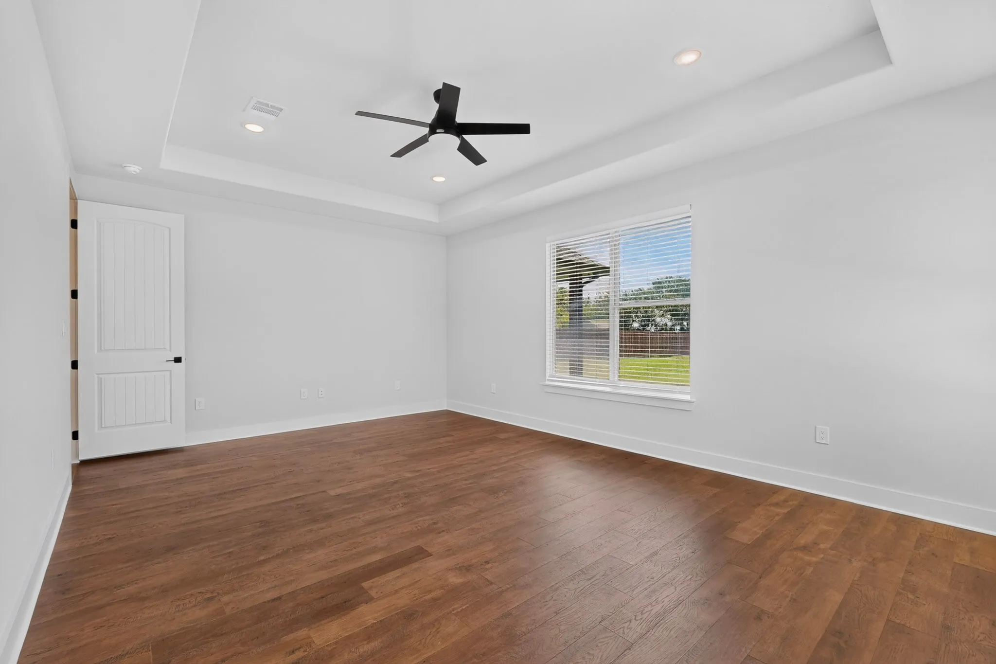 Wood-finish flooring, white walls, and a tray ceiling with recessed lighting