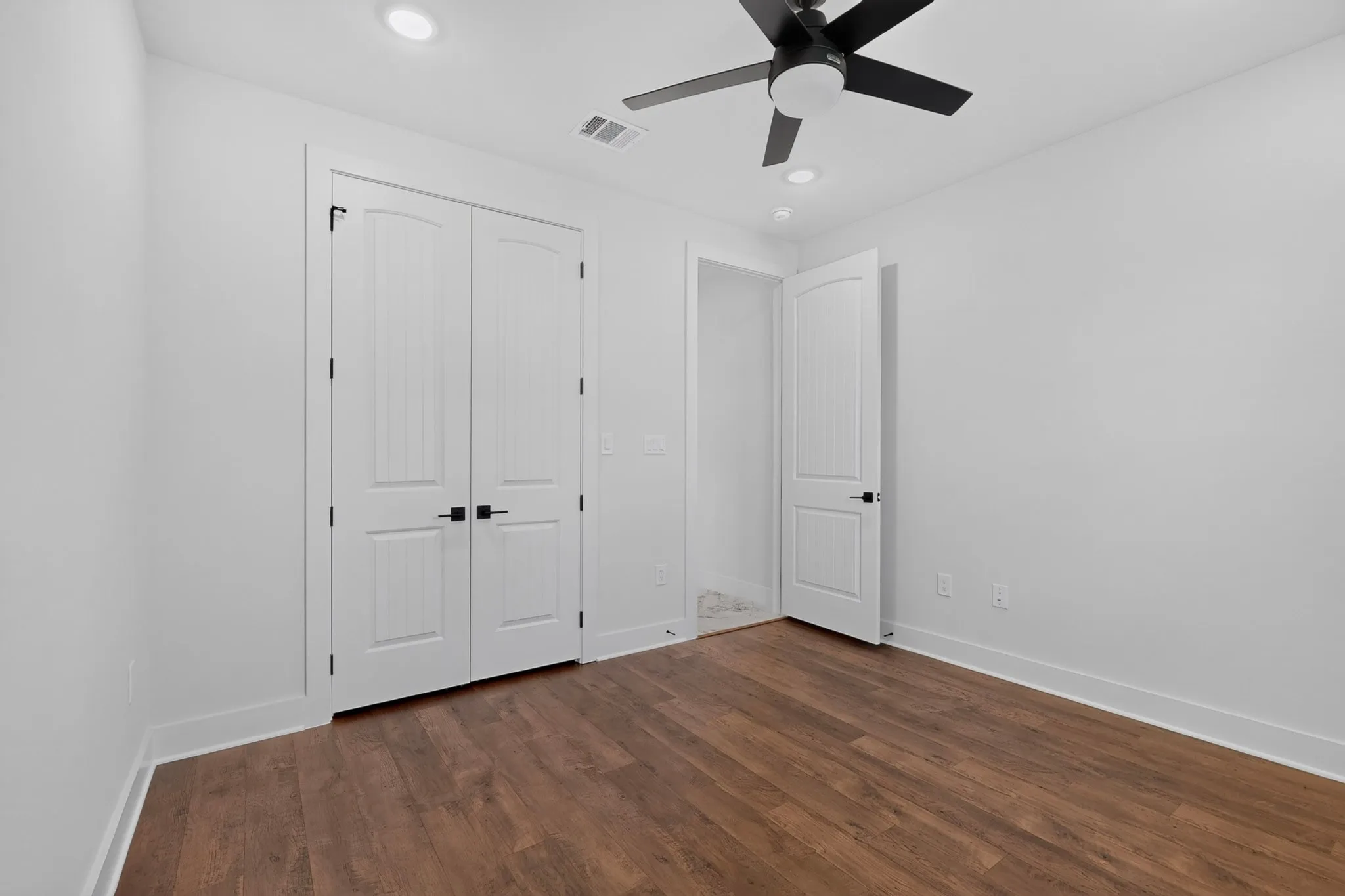 Wood-finish flooring, recessed lighting, ceiling fan with light, and white paneled doors with matte black hardware