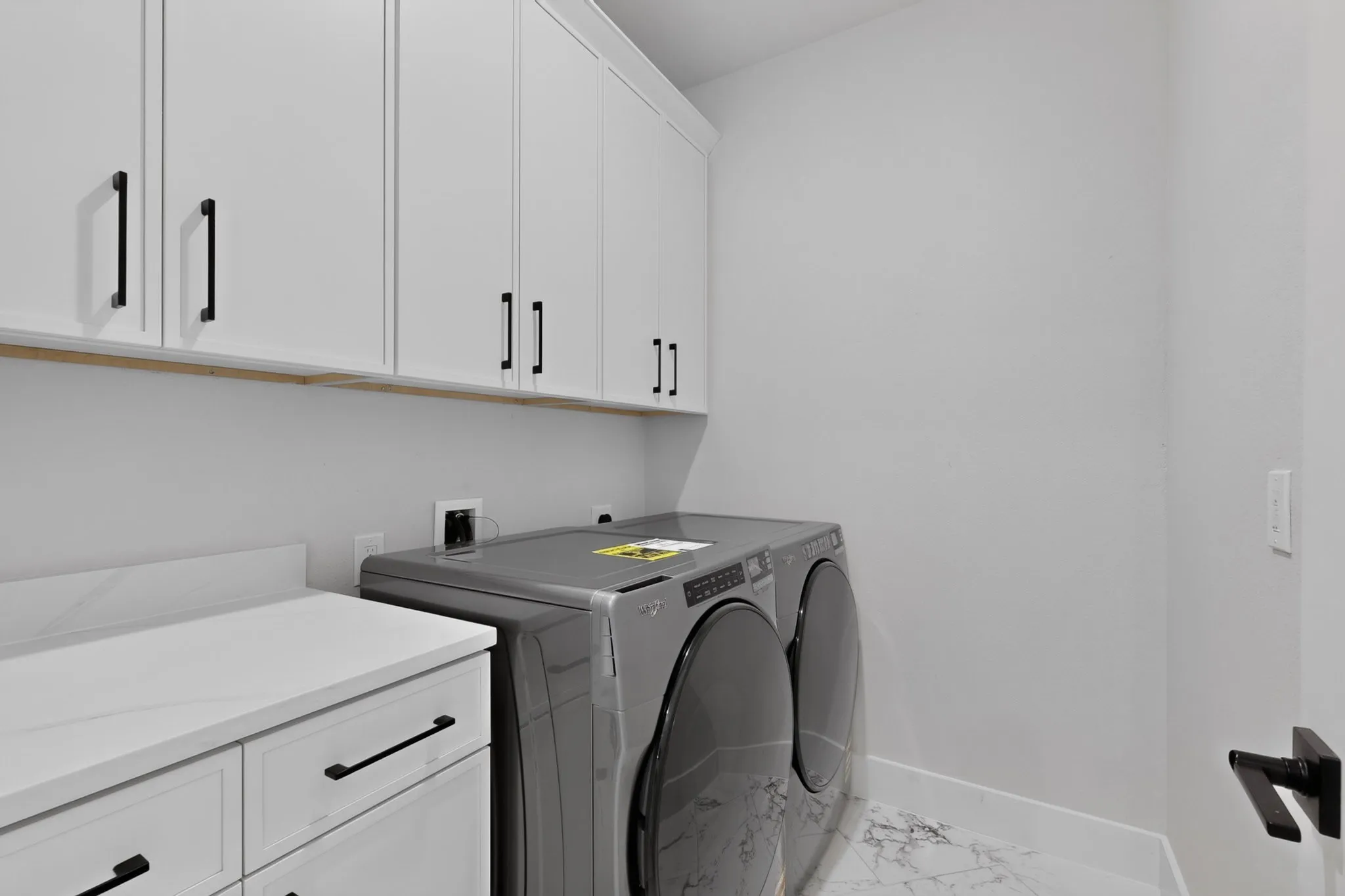 White shaker-style cabinetry with black hardware, white countertop, and marble-look flooring