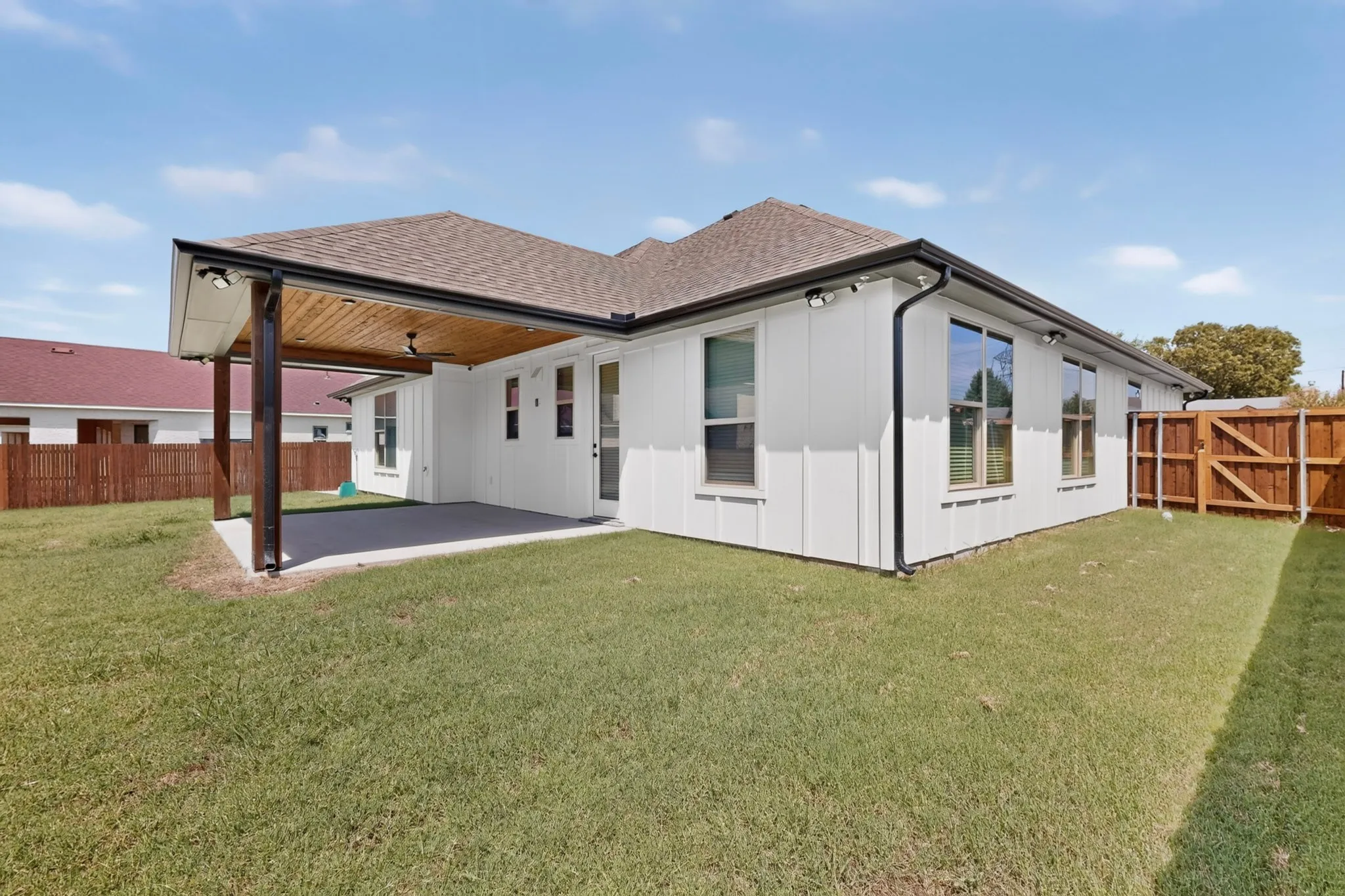 White board-and-batten exterior with dark trim and a covered patio featuring a wood-finish ceiling