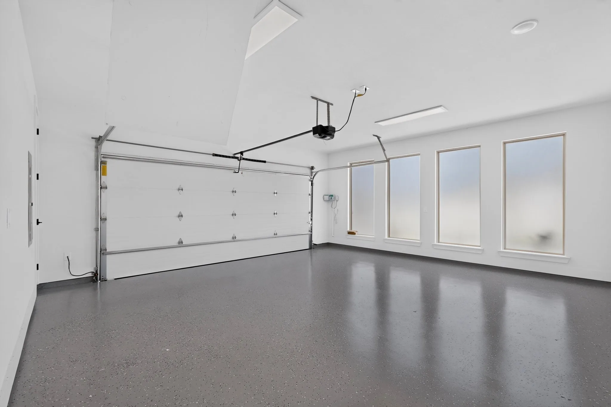 Spacious garage with an automatic overhead door, four transom windows, recessed lighting, and an epoxy-coated concrete floor