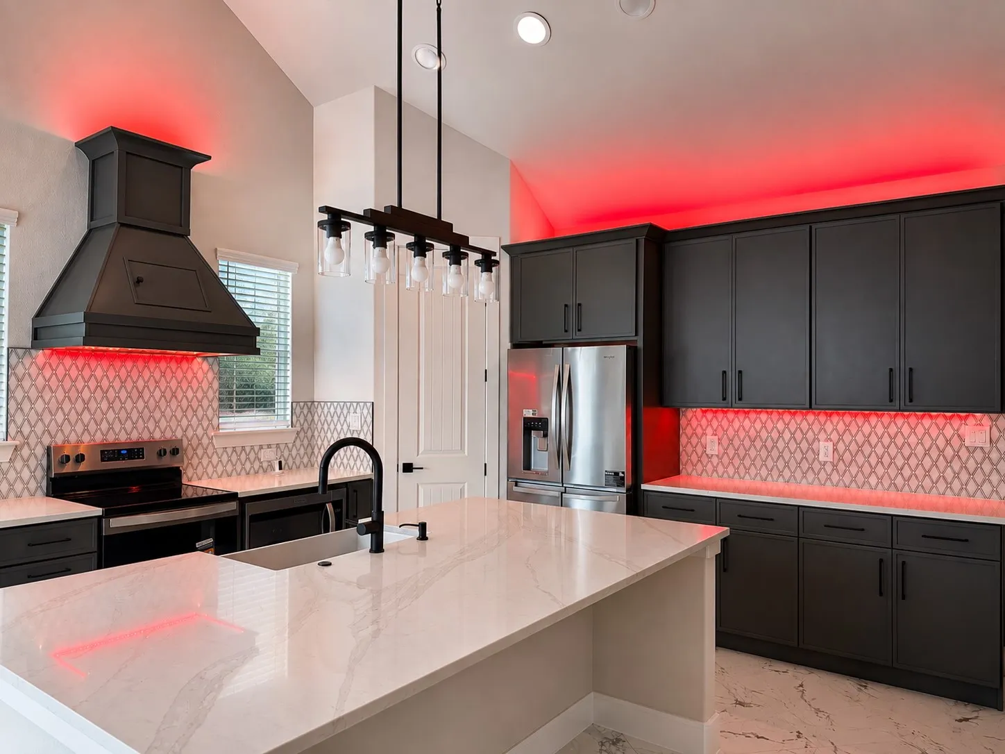 Gourmet kitchen featuring dark cabinetry, a built-in range hood, stainless steel appliances, and a mosaic tile backsplash
