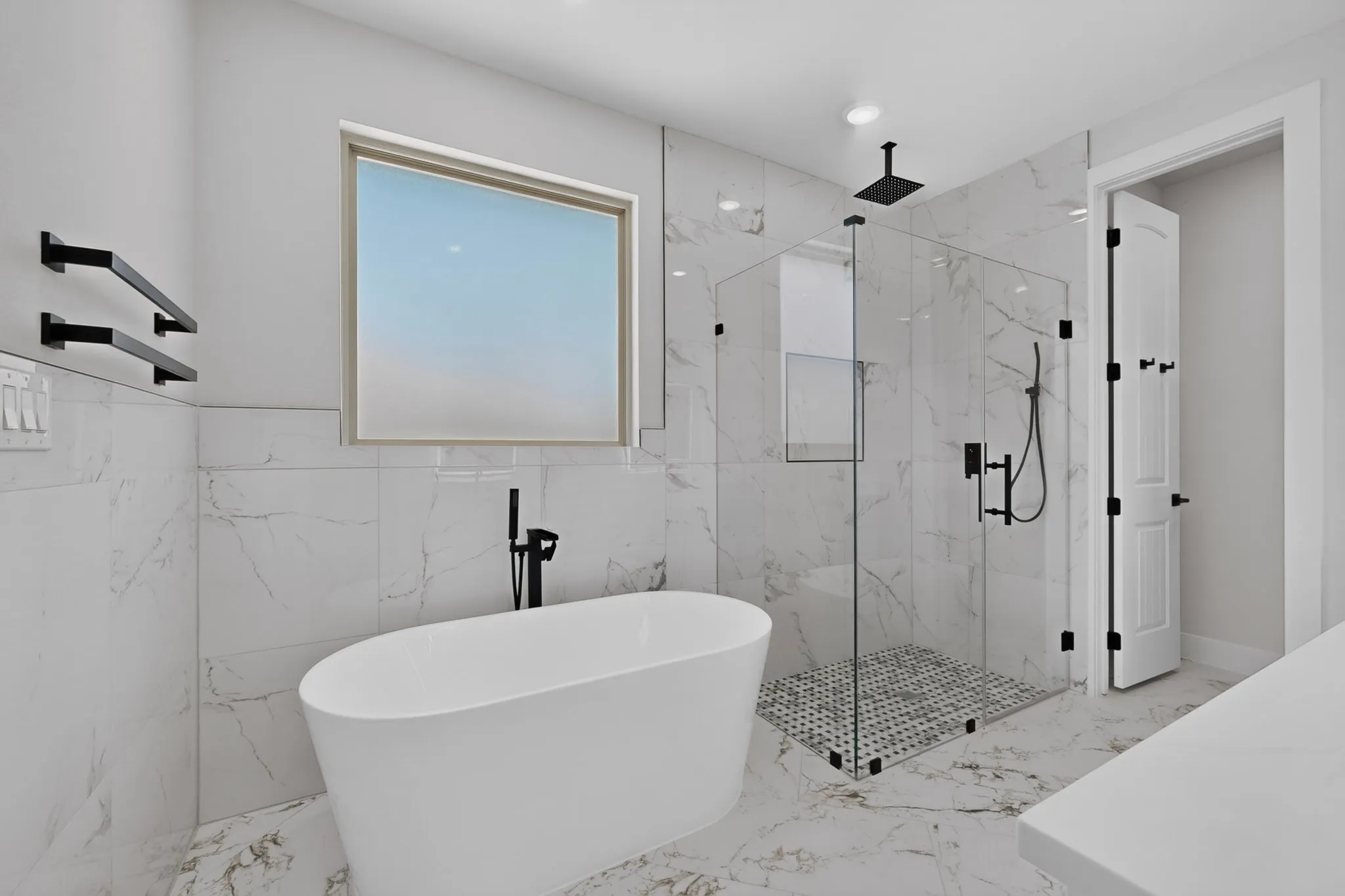Freestanding soaking tub with a floor-mounted faucet, walk-in glass shower enclosure, rainfall showerhead, and marble-look wall and floor tiling