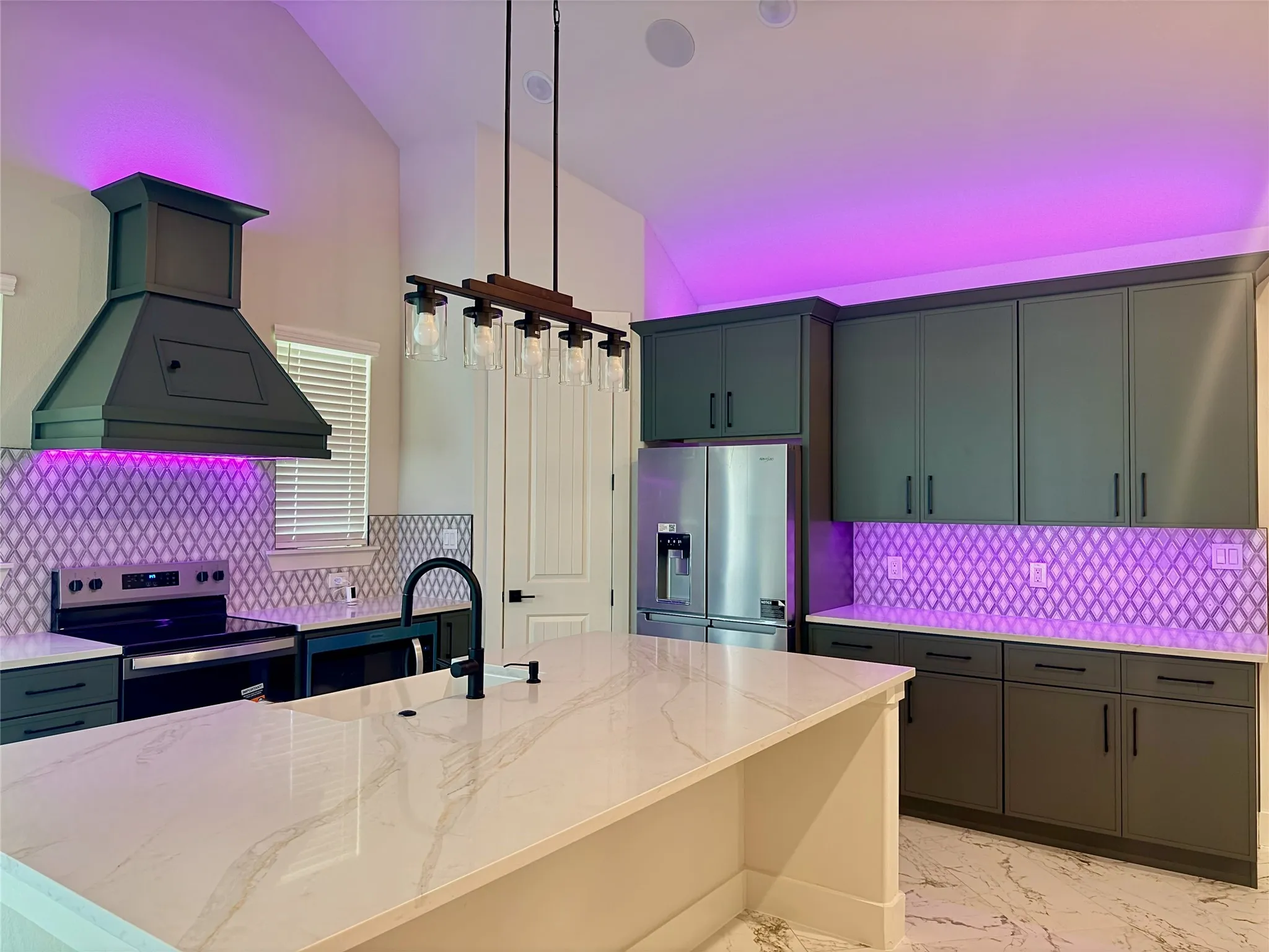 Kitchen featuring a large central island with a light-toned countertop, a range hood, dark cabinetry, and a patterned tile backsplash