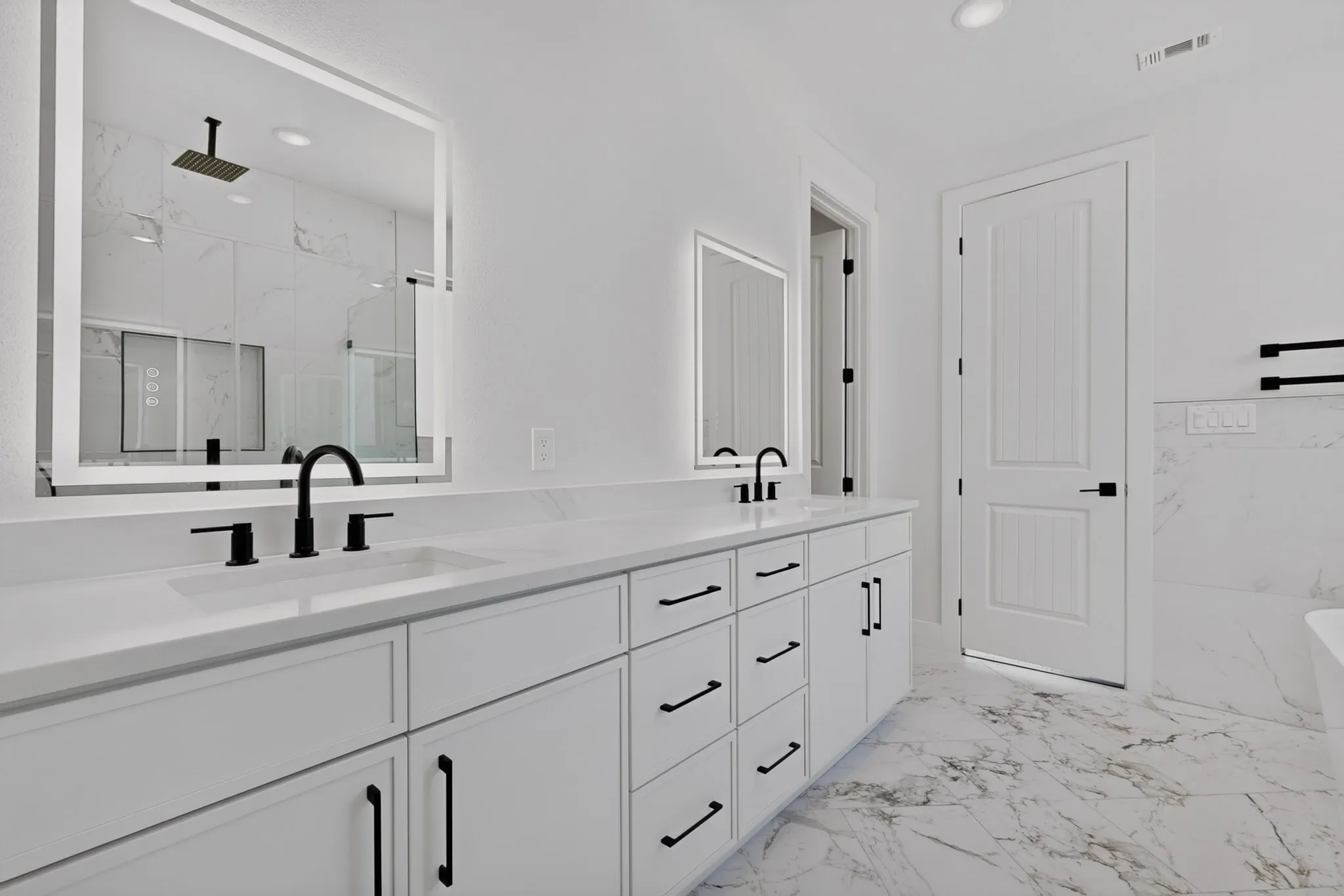 Dual-sink vanity with white cabinetry, black hardware, and an illuminated mirror