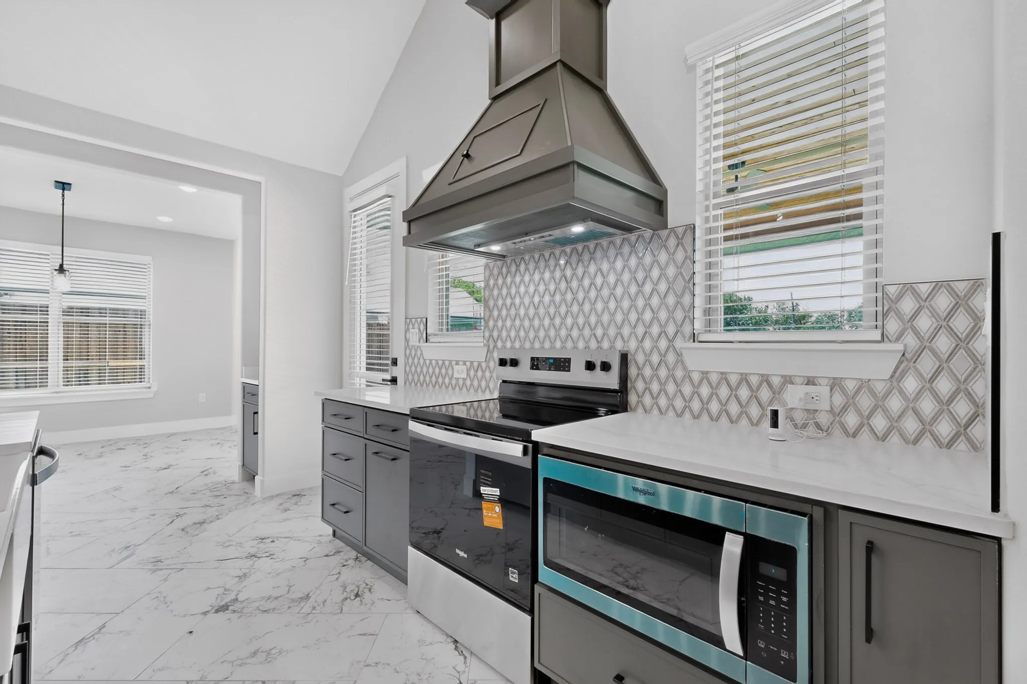 Vaulted ceiling kitchen featuring stainless steel appliances, patterned tile backsplash, quartz countertops, and gray cabinetry