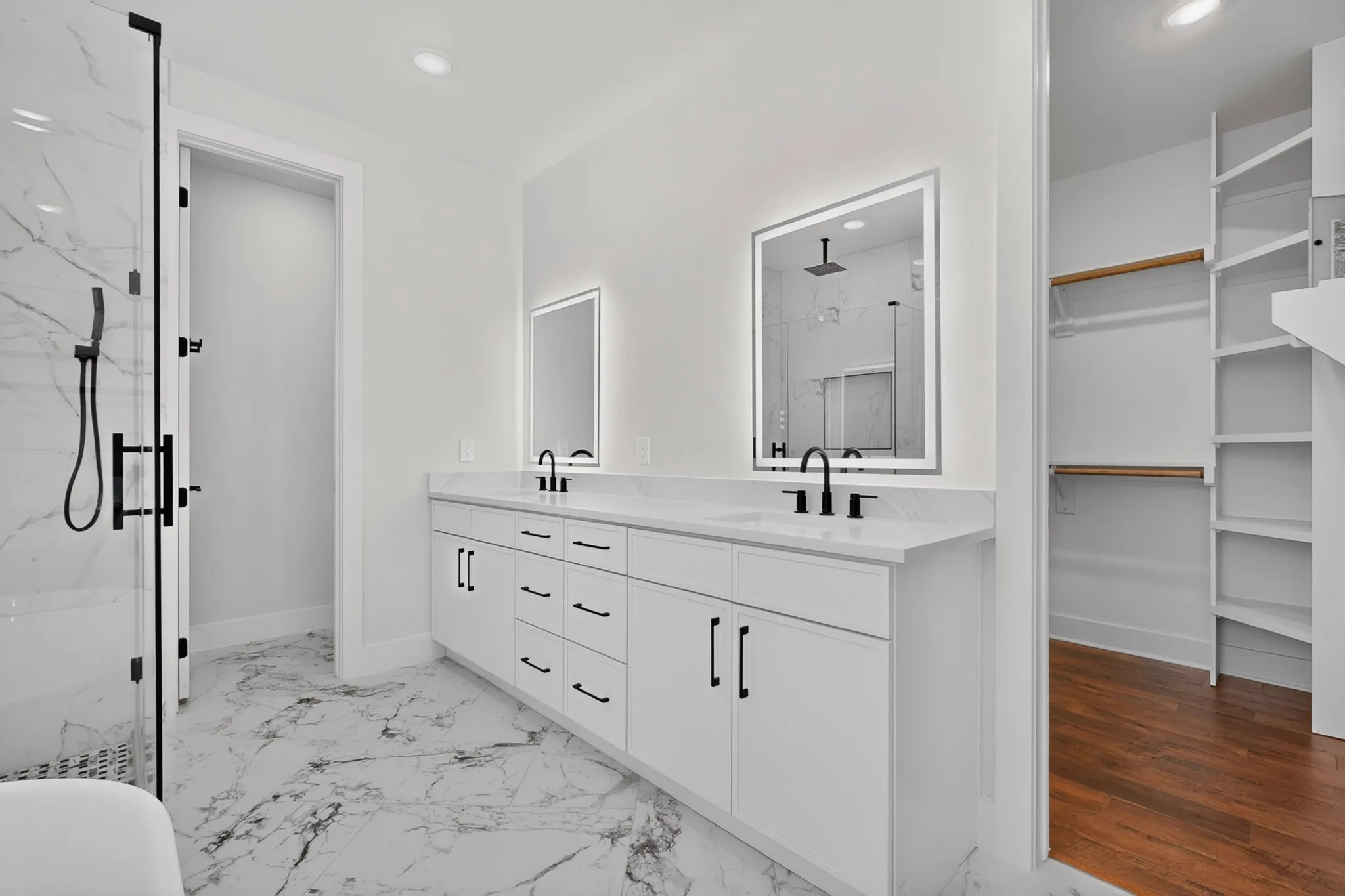 Dual vanity with white cabinetry and black hardware, stone countertops, two illuminated mirrors, walk-in shower with black-framed glass enclosure, and marble-look tile flooring