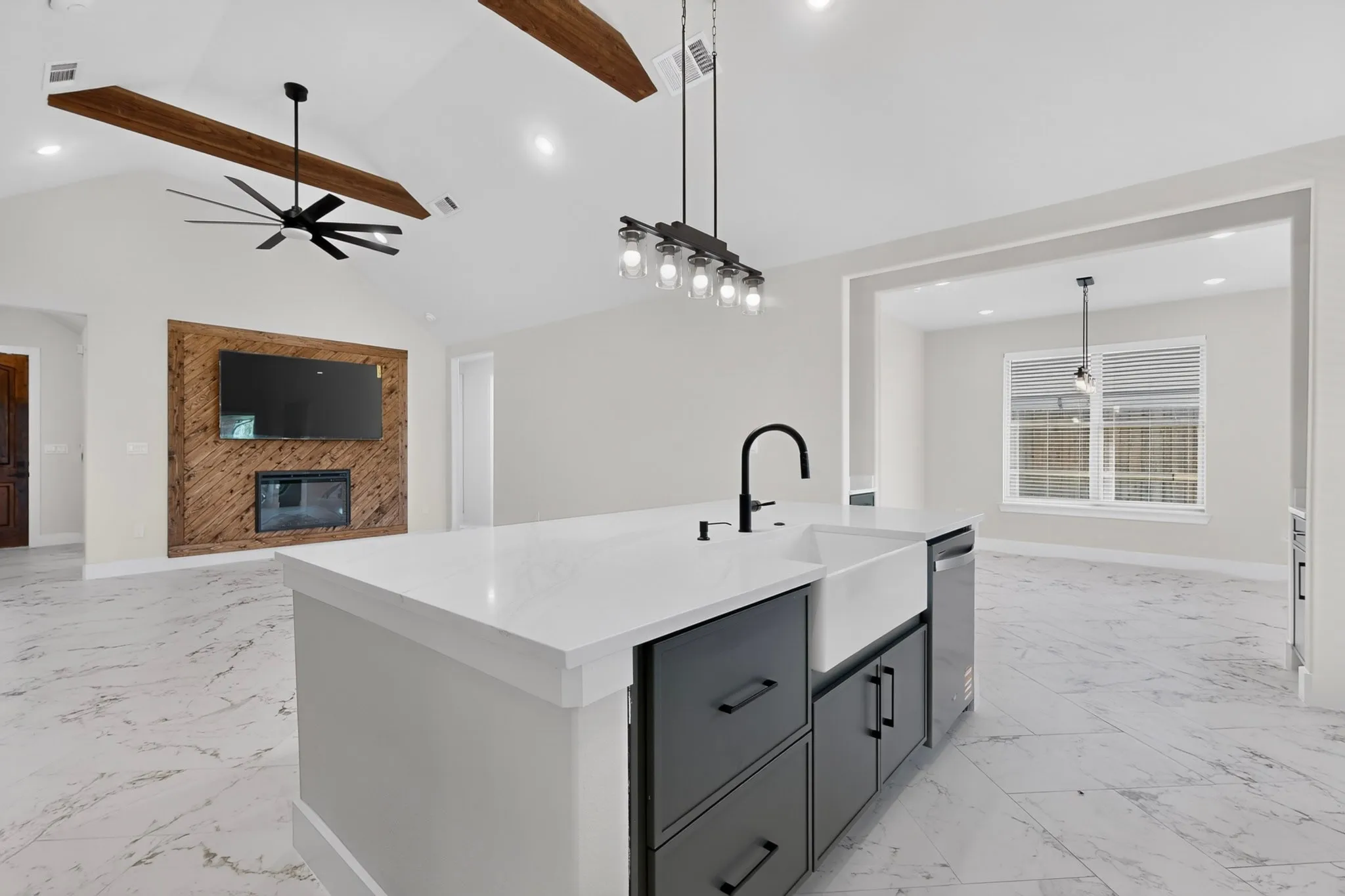 Spacious kitchen island with a farmhouse sink and matte black faucet, integrated dishwasher, vaulted ceiling with exposed wood beams, and a modern ceiling fan