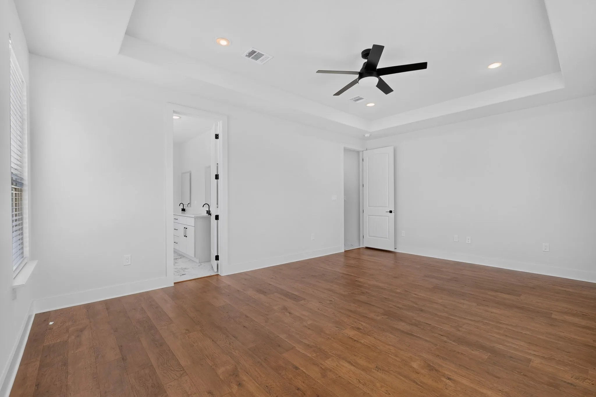 Wood-finish flooring throughout, tray ceiling with recessed lighting, and a matte black ceiling fan