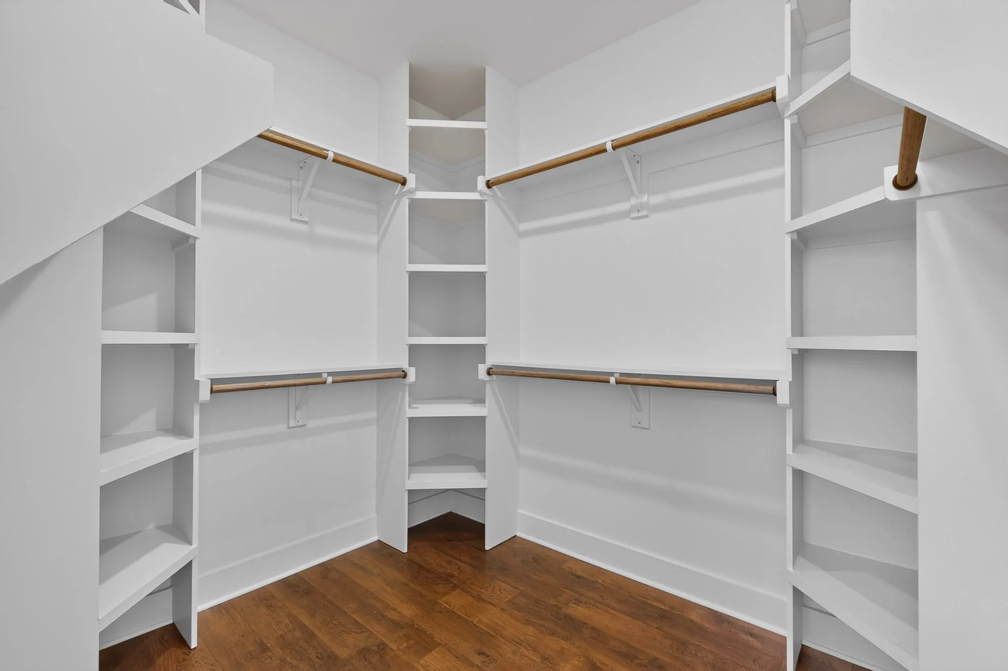 Walk-in closet featuring built-in shelving, multiple hanging rods, and wood-finish flooring