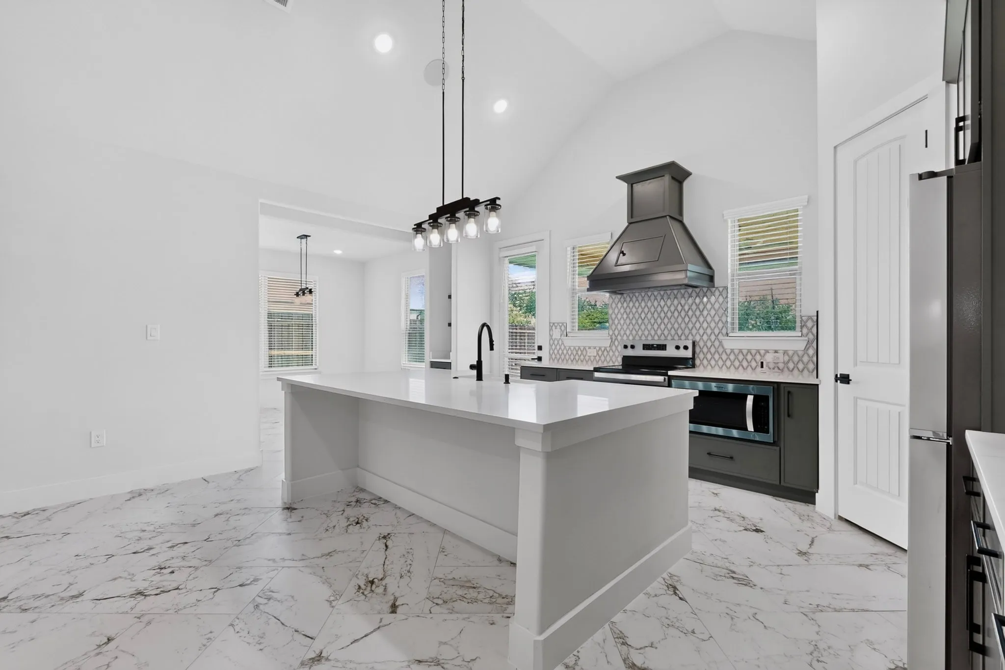 Kitchen featuring a vaulted ceiling, large central island with a sink, stainless steel appliances, decorative range hood, and tile backsplash