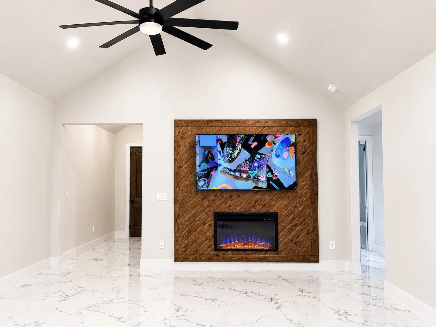 Vaulted ceiling featuring a ceiling fan and recessed lighting, a wood-paneled accent wall, a built-in electric fireplace, and white-veined flooring