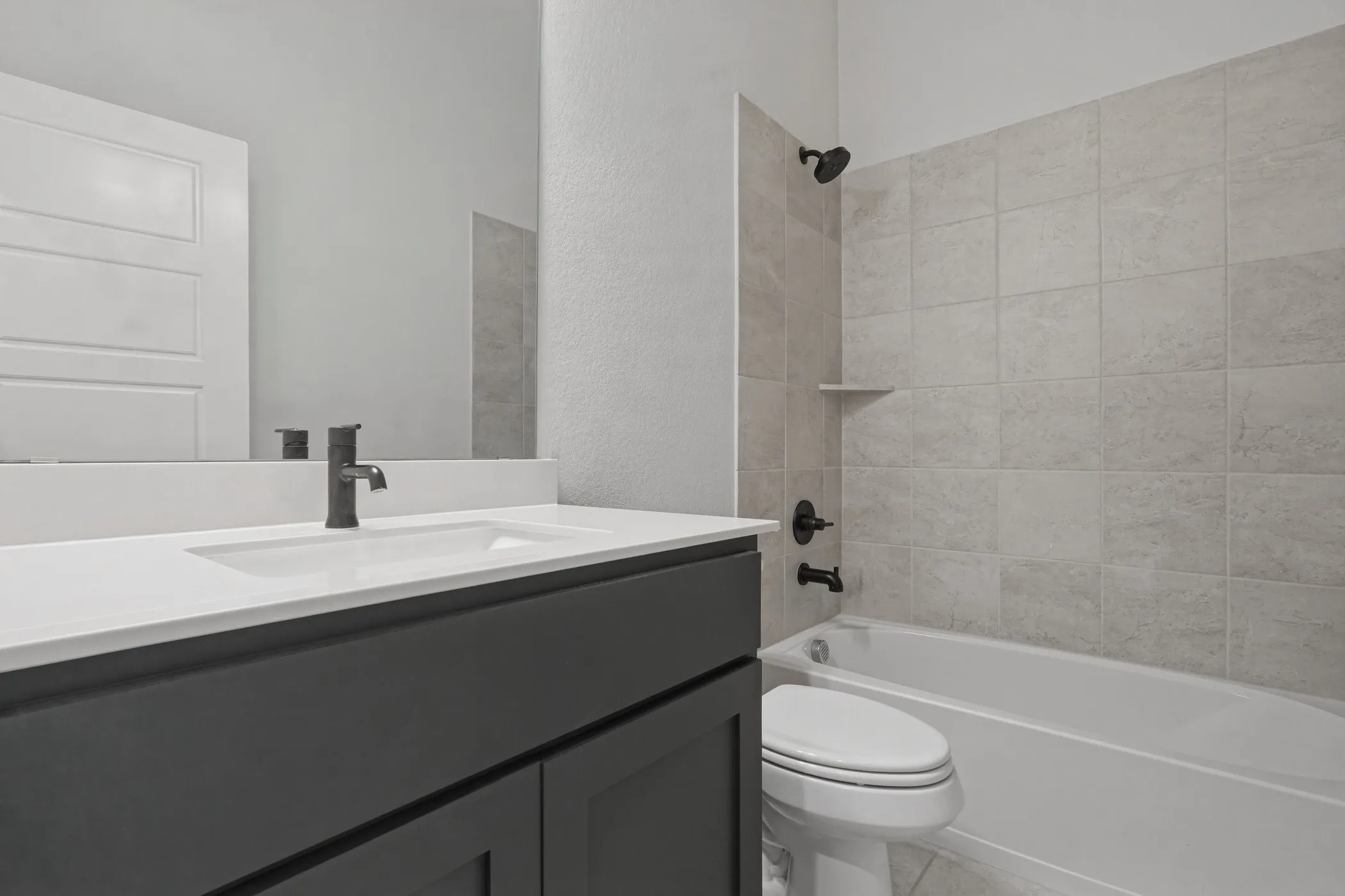 Vanity with an integrated rectangular sink, dark cabinetry, and a light countertop paired with a tiled tub/shower combination featuring matte black fixtures