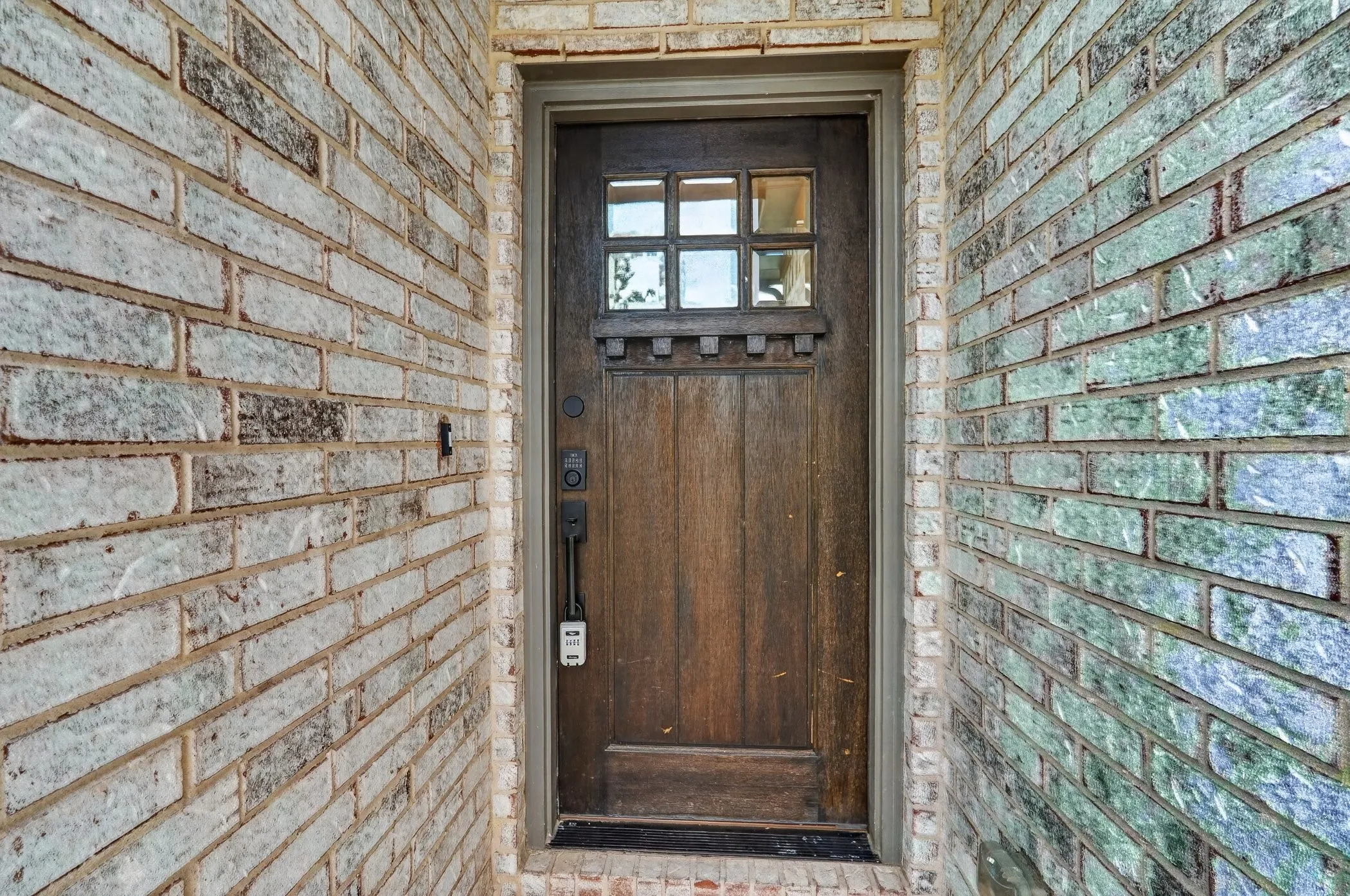 Wood-finish entry door with upper grid glass paneling, complemented by a brick exterior featuring varied tones