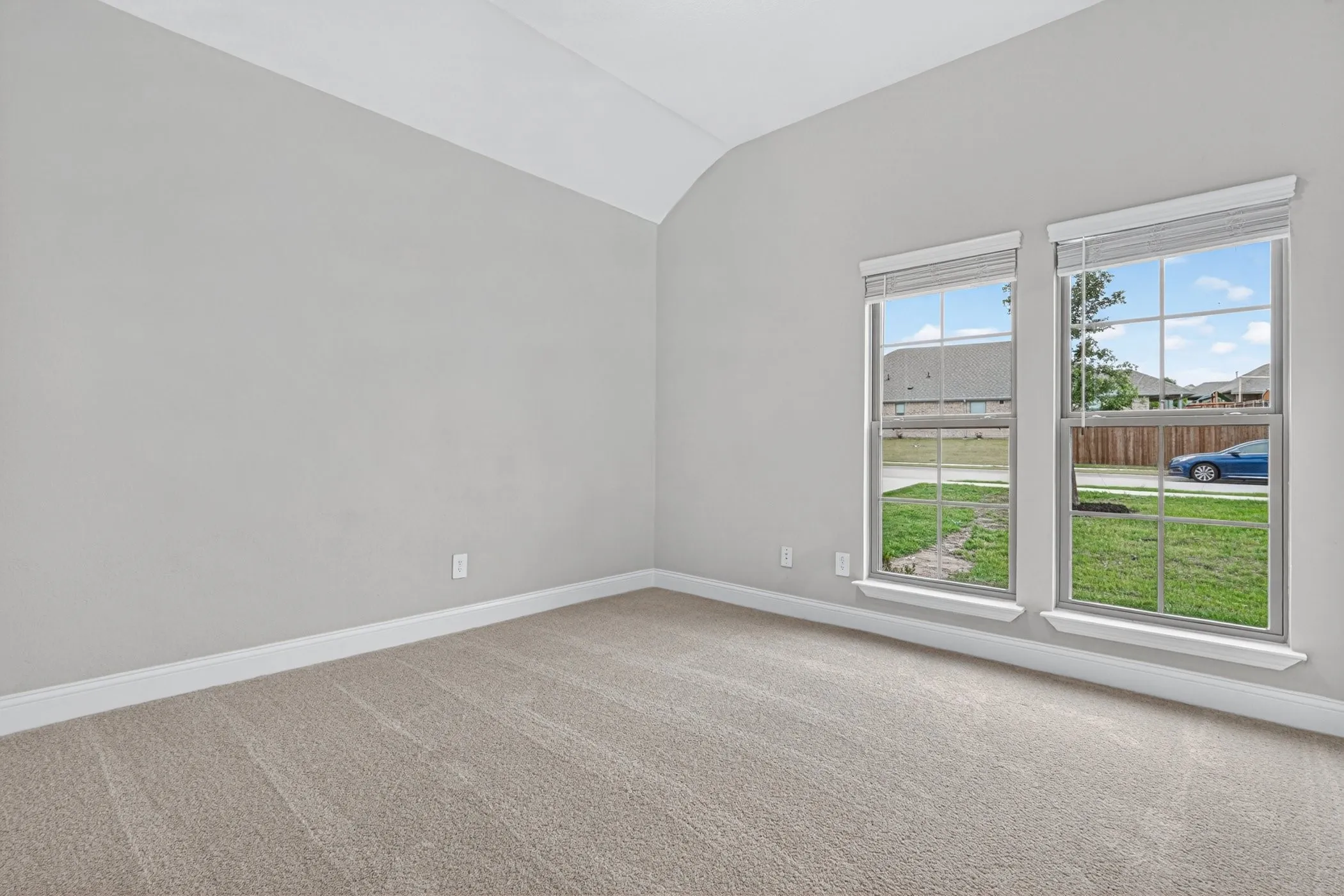Vaulted ceiling accentuates the spacious room with neutral-toned carpet and light gray walls