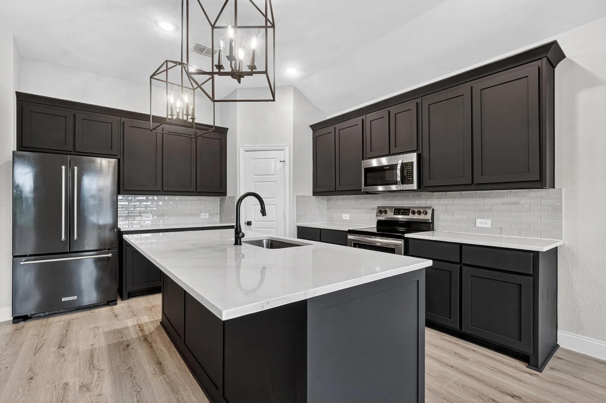 Kitchen featuring an island with sink, dark cabinetry, light countertops, subway tile backsplash, and wood-finish flooring