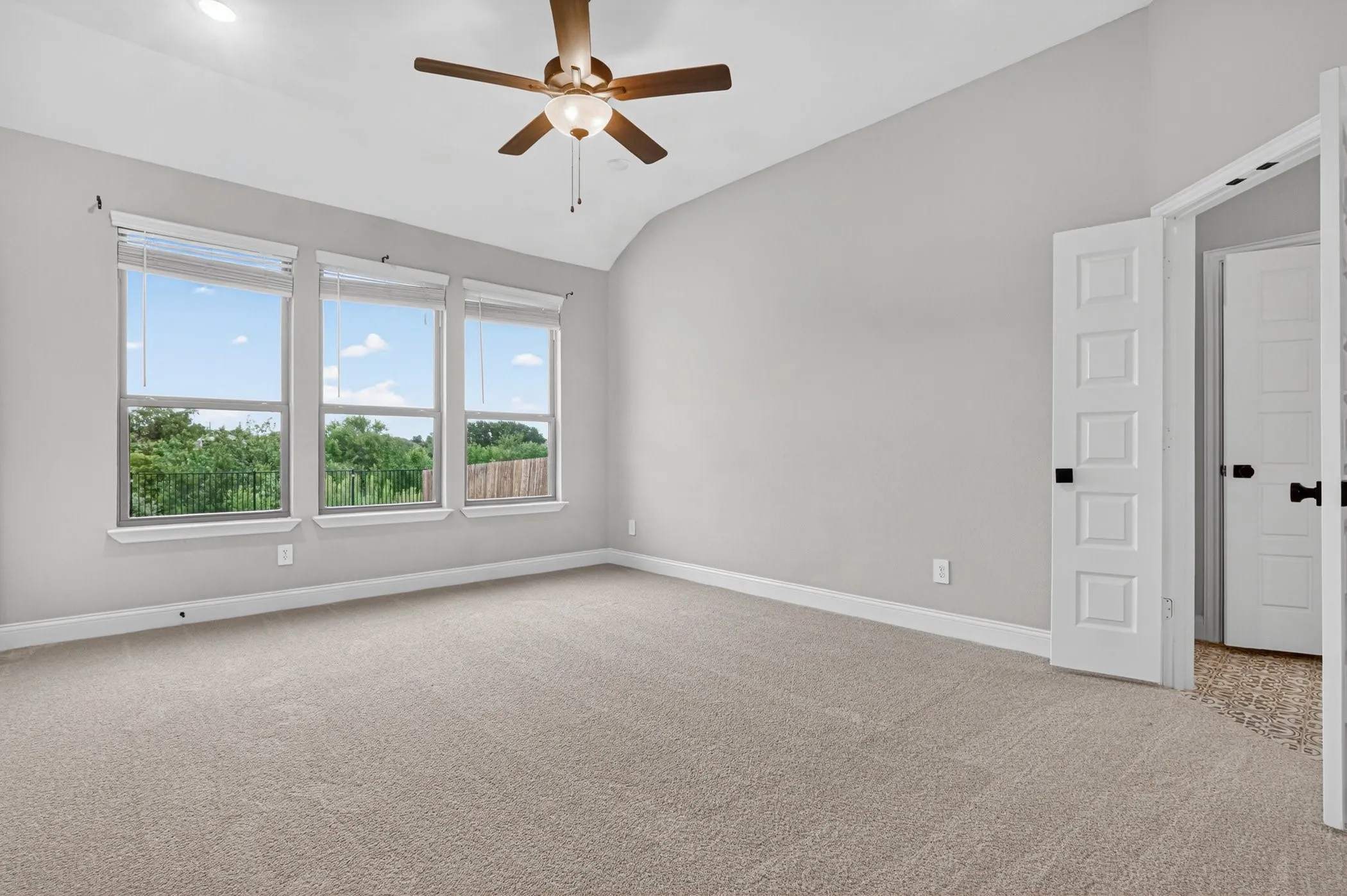 Vaulted ceiling with a ceiling fan, three large windows, carpet flooring, and paneled doors with black hardware