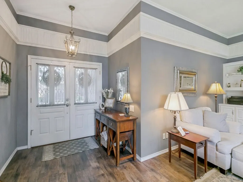 Double entry doors with decorative glass inserts, LVP wood flooring, overhead chandelier, intricate crown molding, and built-in cabinetry