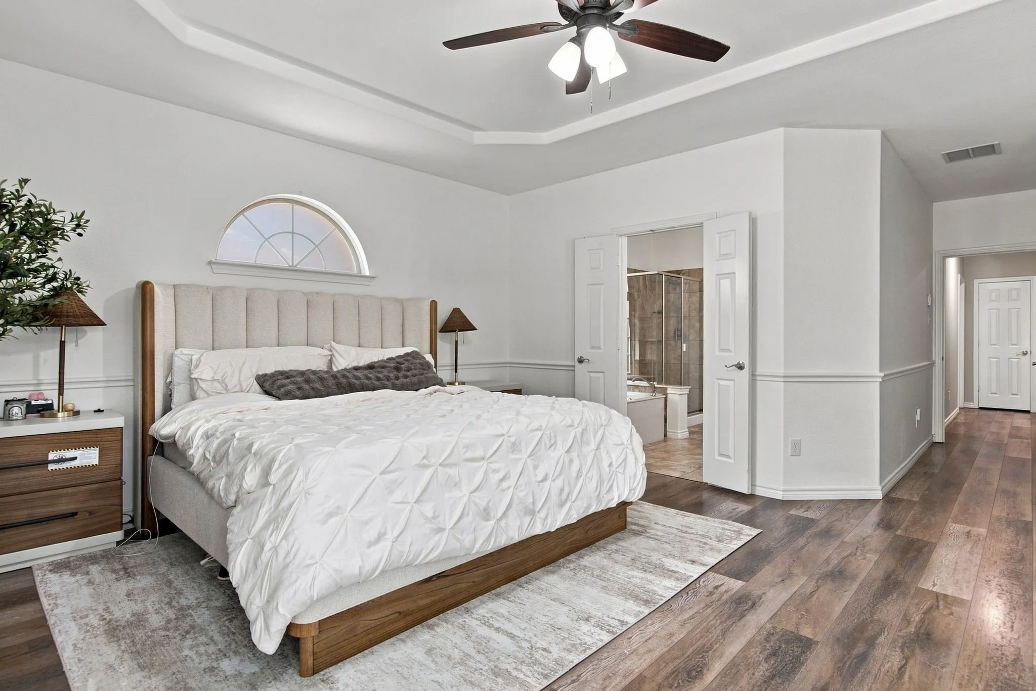 Tray ceiling with a ceiling fan, arched window, wood-finish flooring, and white paneled doors