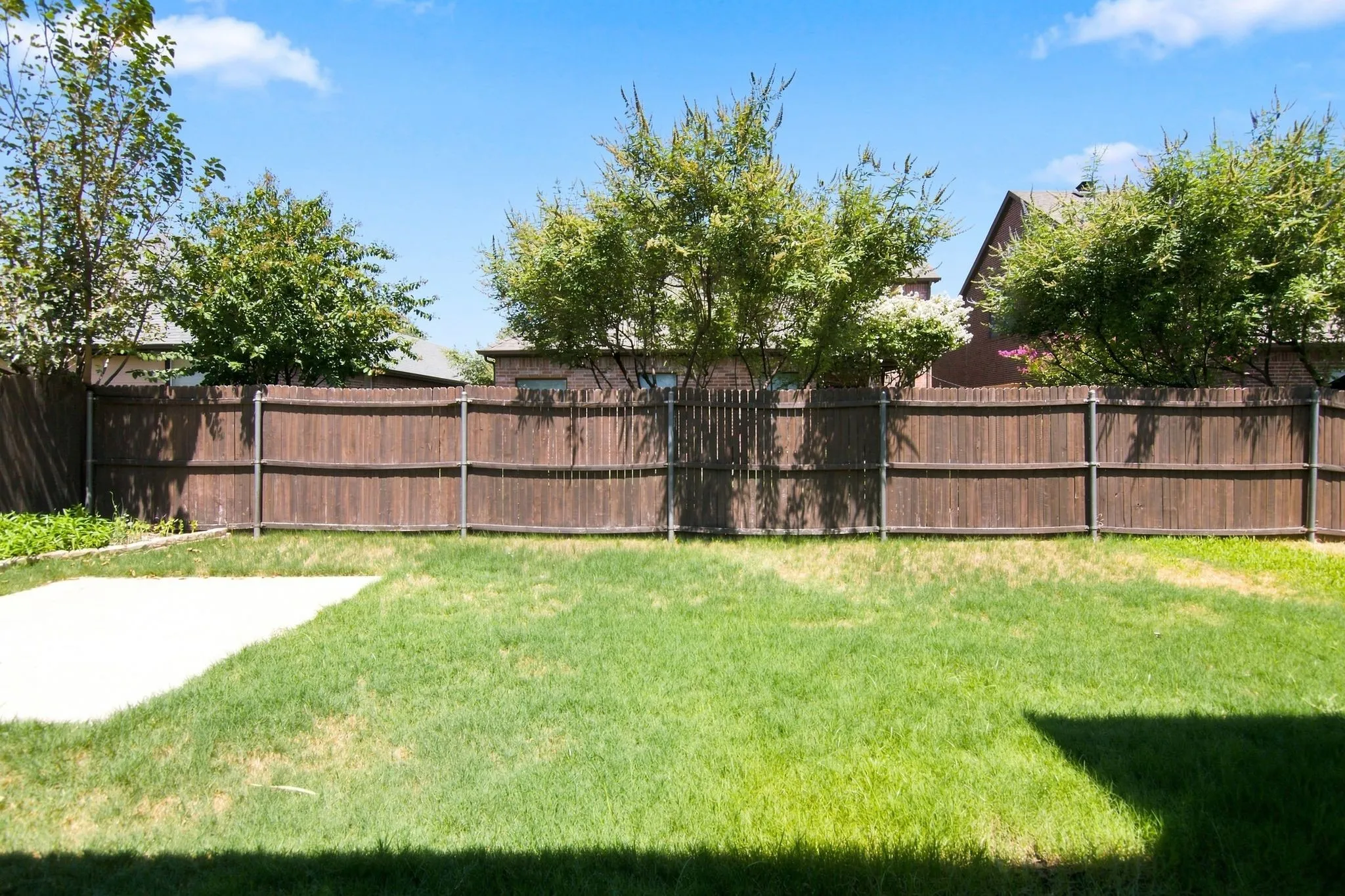 Expansive backyard featuring a lush lawn, privacy fencing, mature trees, and a concrete patio