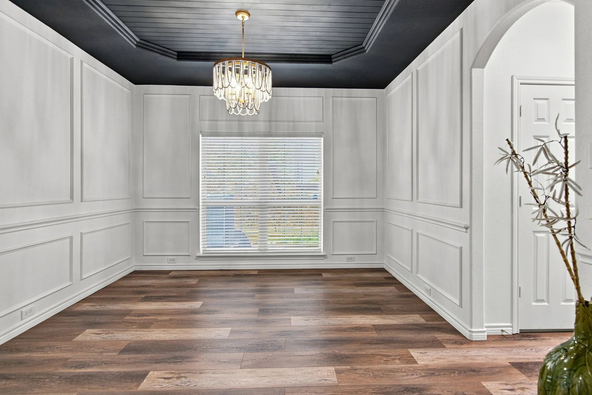 Wood-finish flooring, wainscoting, decorative ceiling, crystal chandelier, and a window with blinds