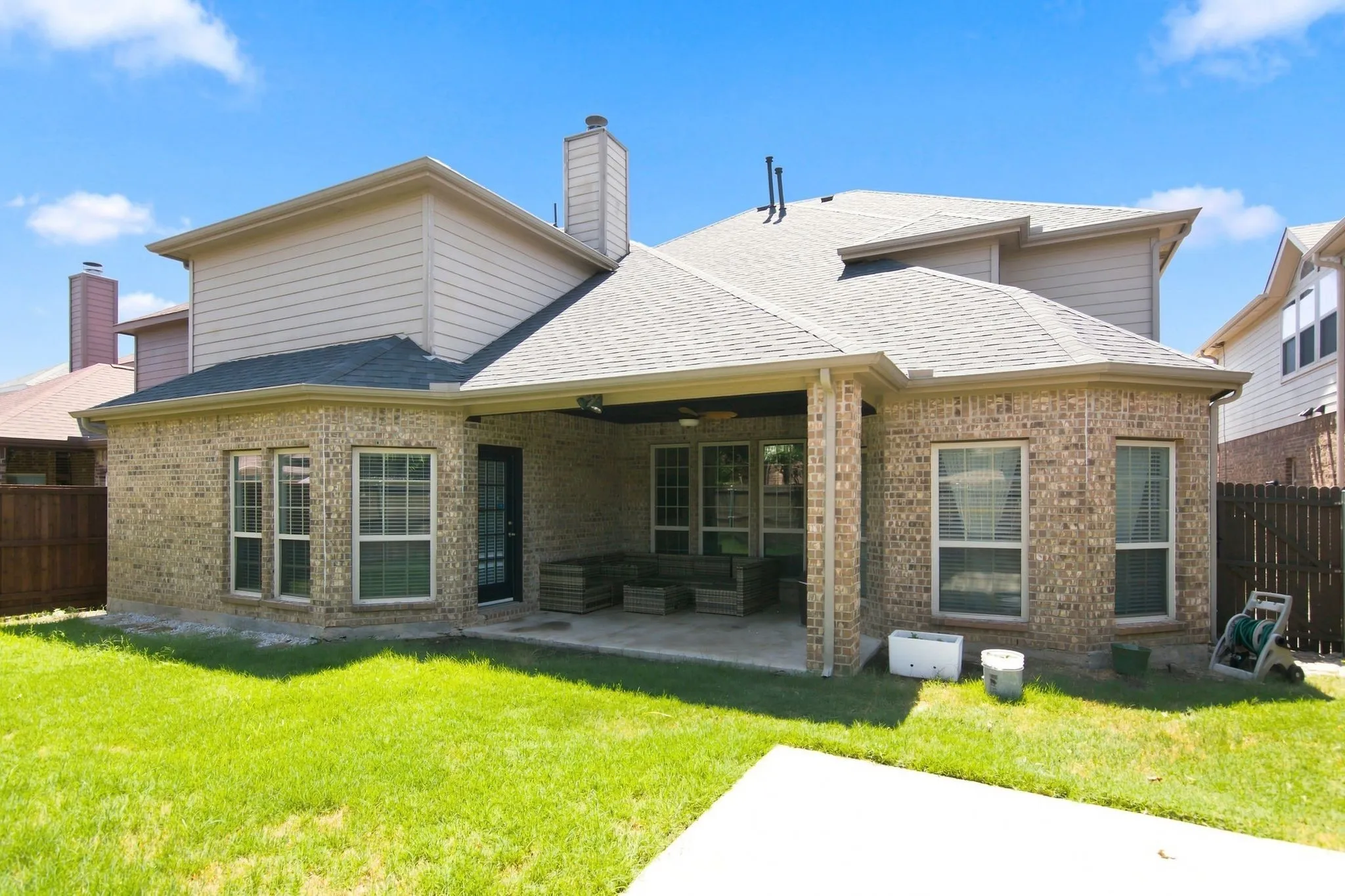 Expansive backyard featuring a manicured lawn, full brick exterior, covered patio, and a privacy fence