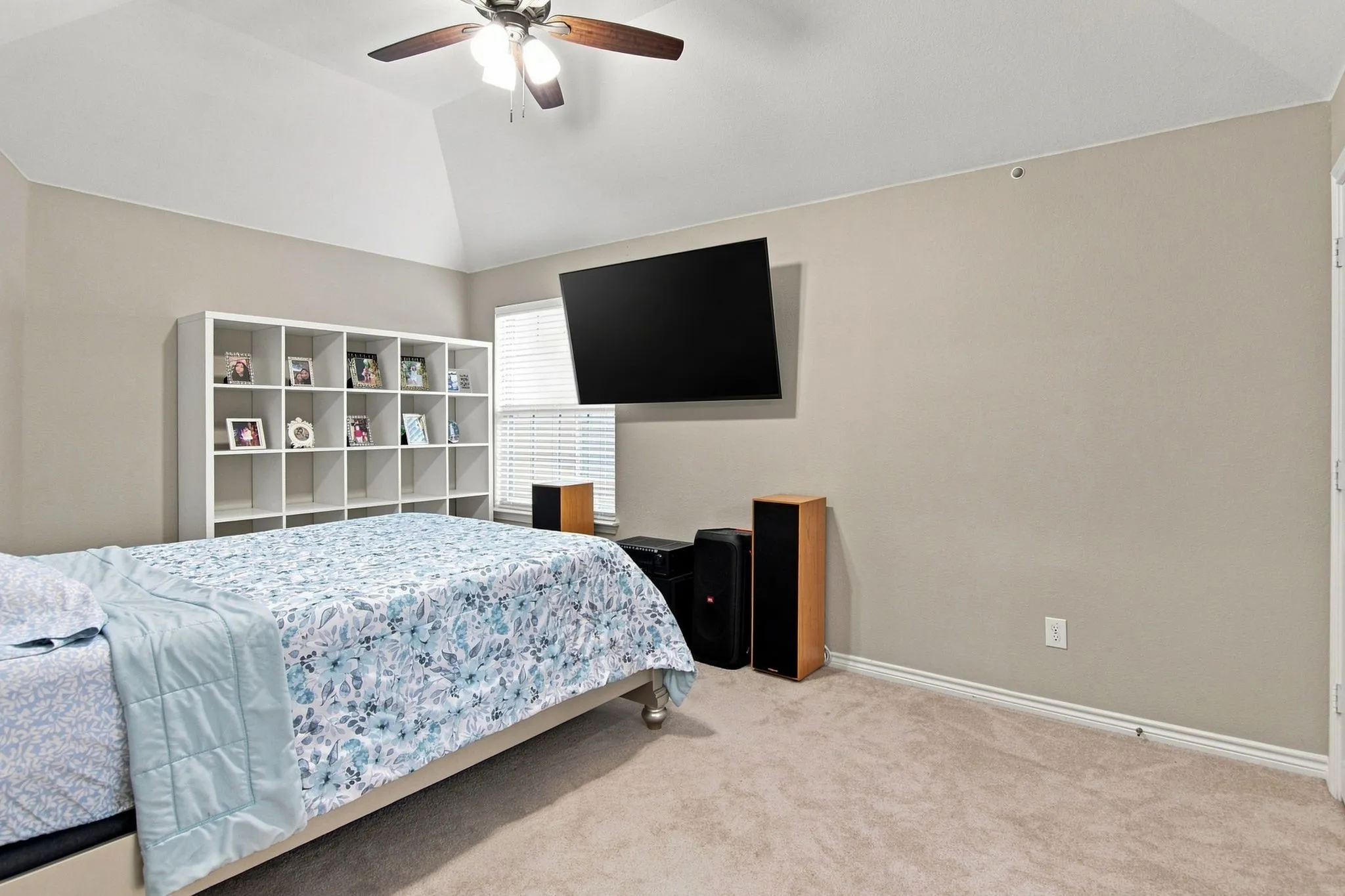 Vaulted ceiling with a ceiling fan, neutral carpet flooring, a wall-mounted flat-screen, and a built-in shelving unit