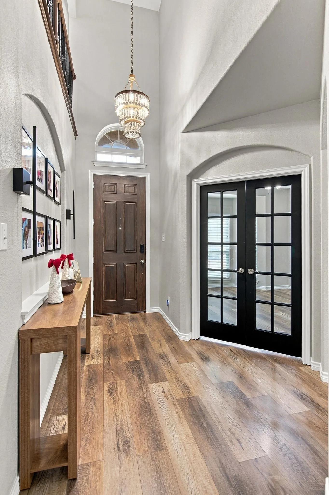 Two-story entryway featuring a tiered chandelier, wood-finish flooring, and black French doors with divided lites