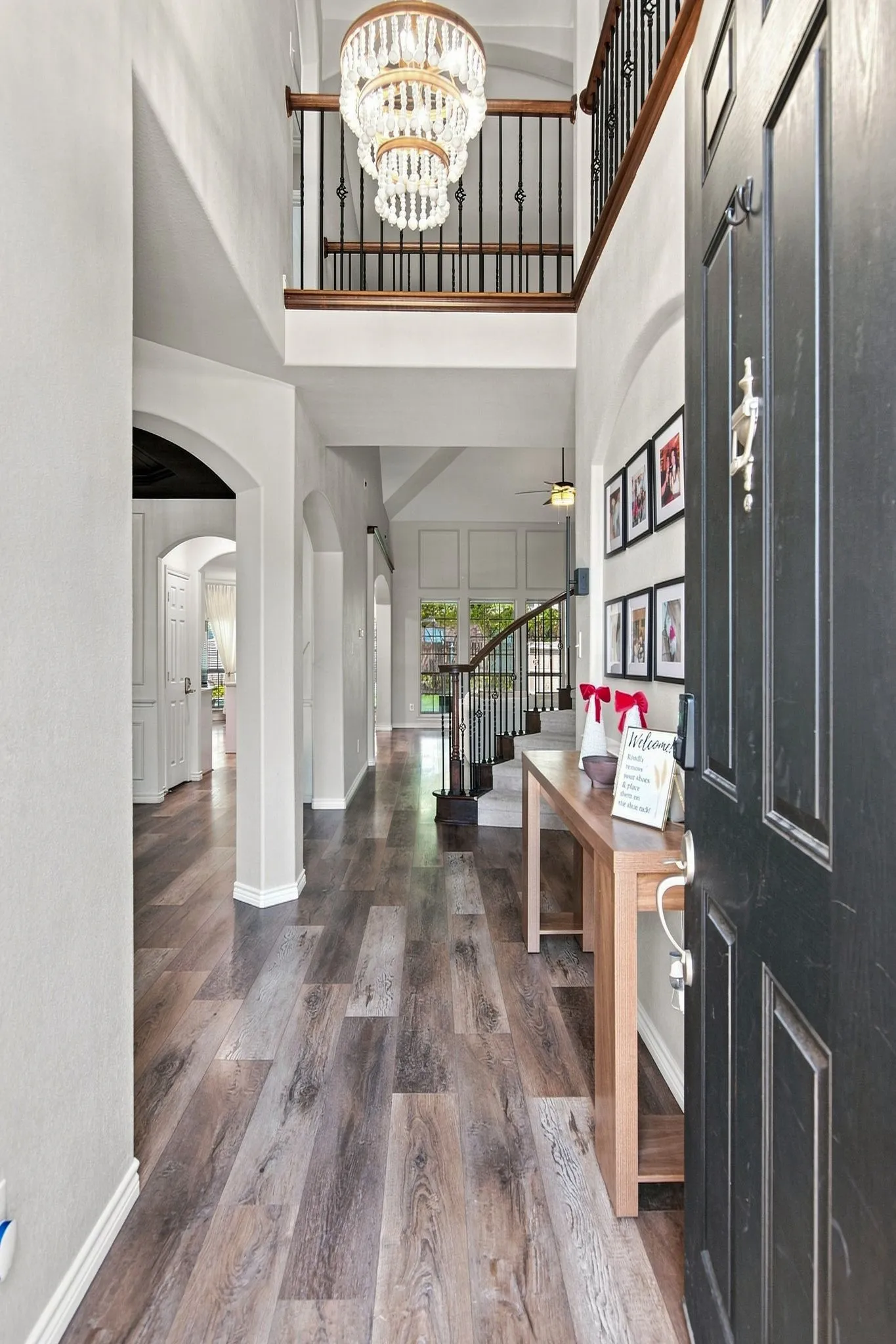 Two-story foyer with wood-finish flooring, arched doorways, a tiered crystal chandelier, and a black wrought iron staircase