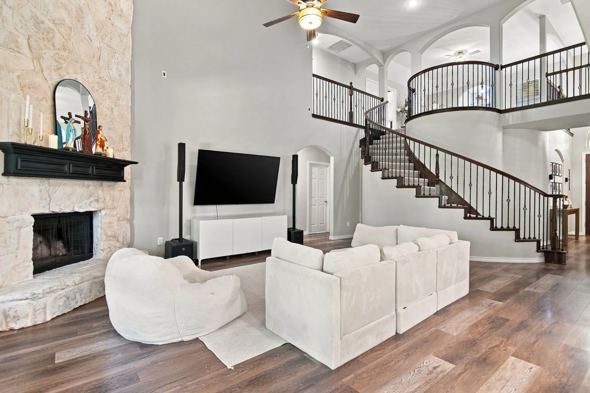 Two-story living area featuring a stone-clad fireplace and hearth, a curved staircase with wrought iron balusters, wood-finish flooring, and arched architectural details
